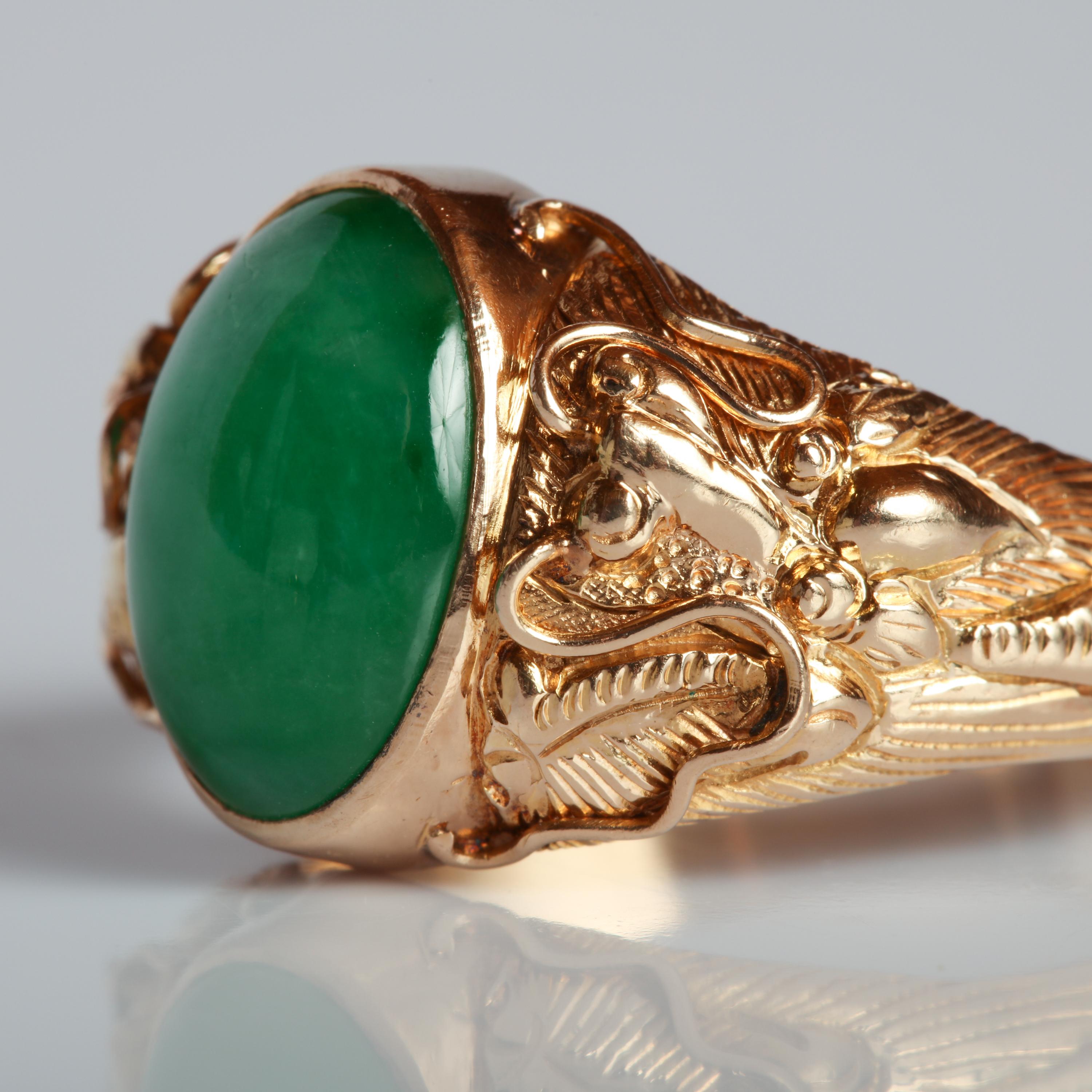 A rich, succulent highly-translucent, and gemmy deep apple green jade cabochon resides within its bezel and is guarded on either side by a pair of exotic, whimsical creatures from the sea. 

The detailing created by the master goldsmith is