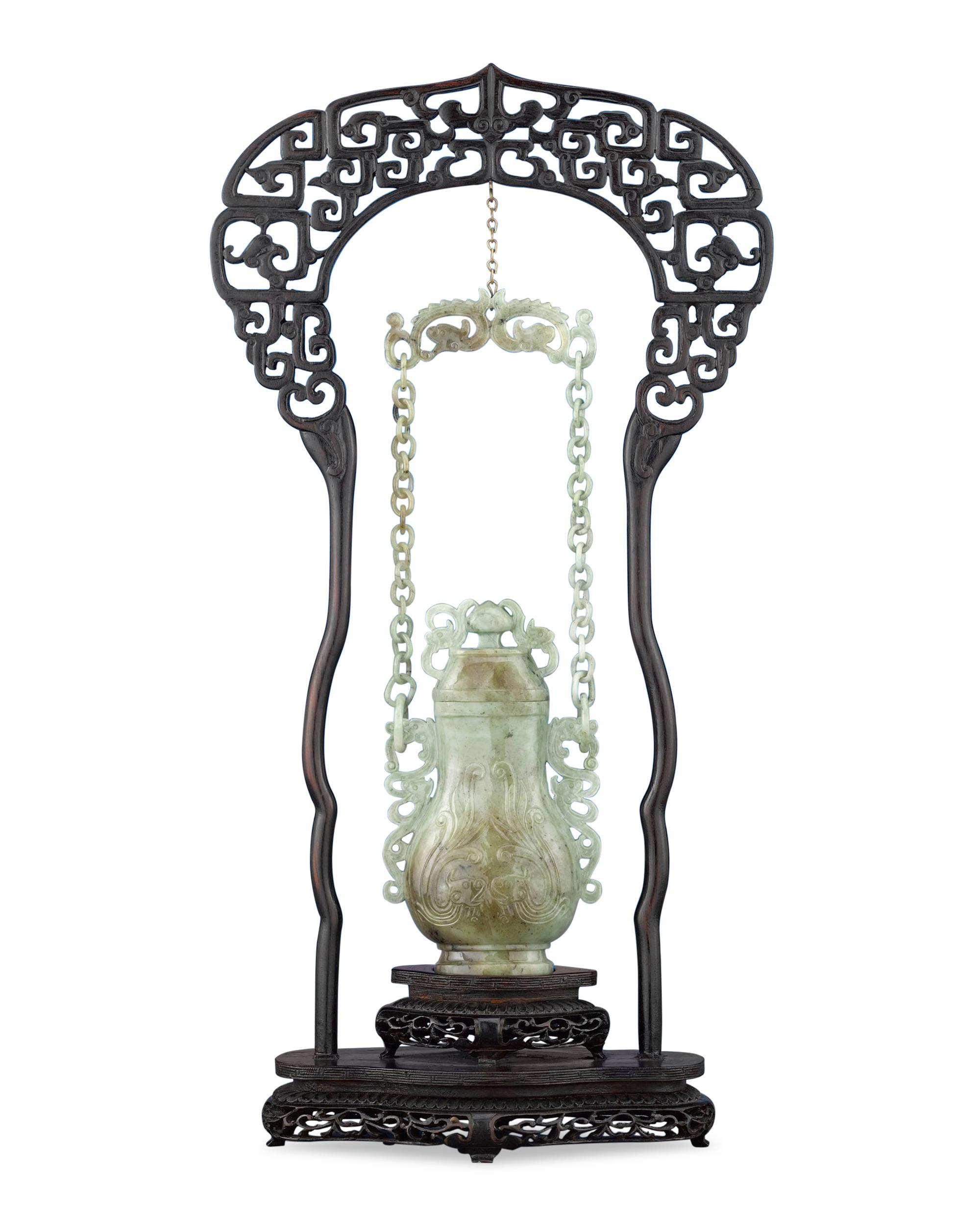 This rare Chinese hanging vase, carved of fine moss-in-snow jade, boasts a host of dragons, the most potent symbols of good fortune in China. Its intricate stand incorporates equally lucky, billowing clouds into its canopy. Hanging vases such as