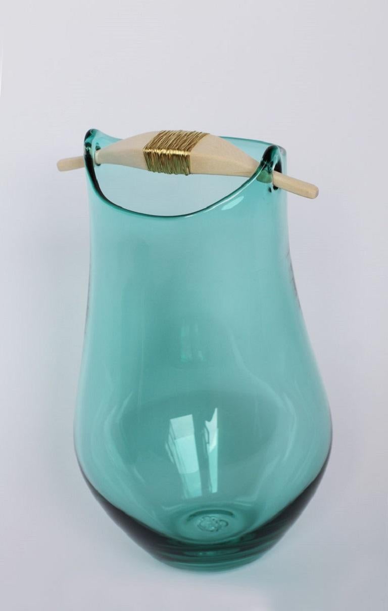 Jade heiki vase, Pia Wüstenberg.
Dimensions: D 20-22 x H 32-40.
Materials: glass, wood, metal wire.
Available in other colors.

Inspired by a simple fix on an old sauna ladle handle, fixed with wire and outright everyday genius. Heiki (named