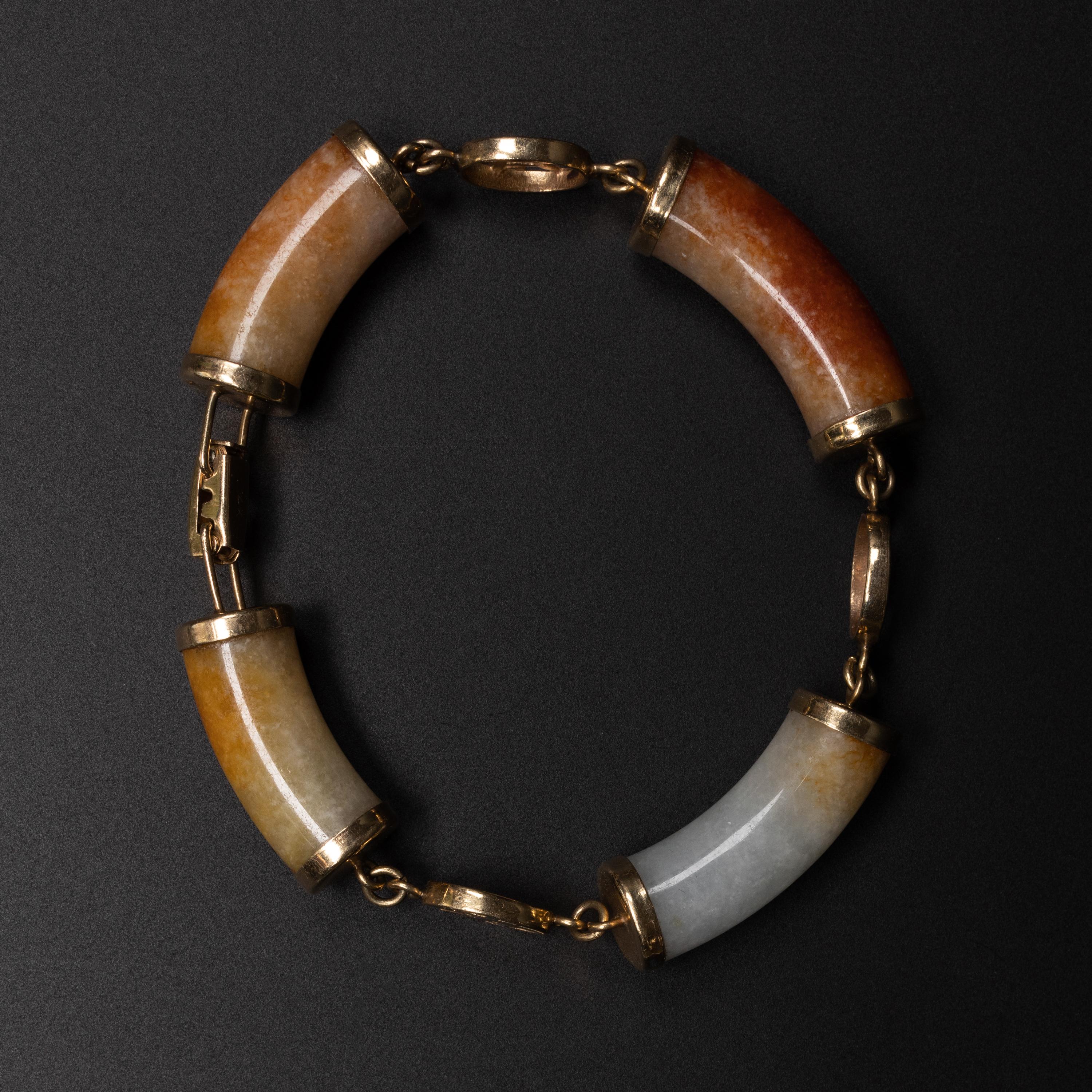 This mid-century (circa 1960) bracelet from iconic Ming's of Hawaii is composed of four hand-carved tubular segments of slightly curved natural and untreated nephrite jade in white, yellowish-brown and russet-red. Each jade segment is capped at both