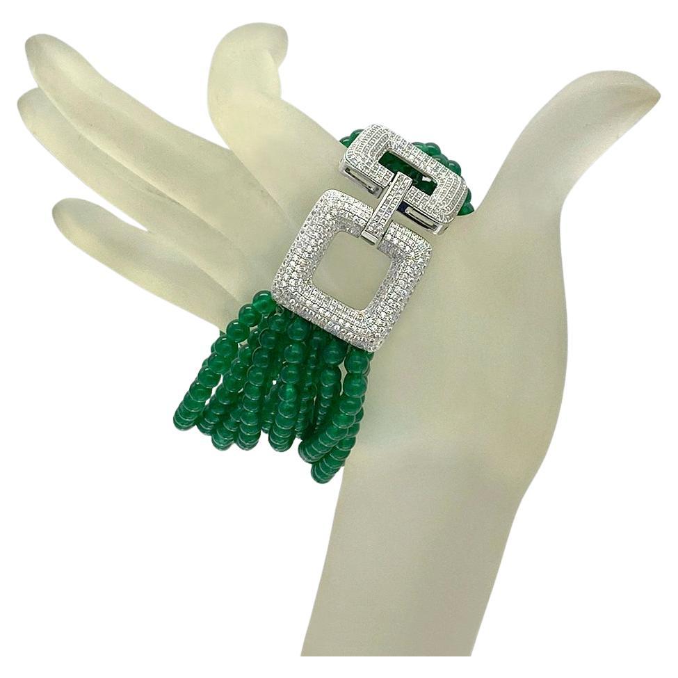 Il s'agit d'un bracelet en jade avec un fermoir de style art déco.  Il est doté d'une paire de grands fermoirs carrés en argent pavé de cz qui contrastent joliment avec douze rangs de perles de jade vert lisse de 4 mm nouées en soie. 

Notre