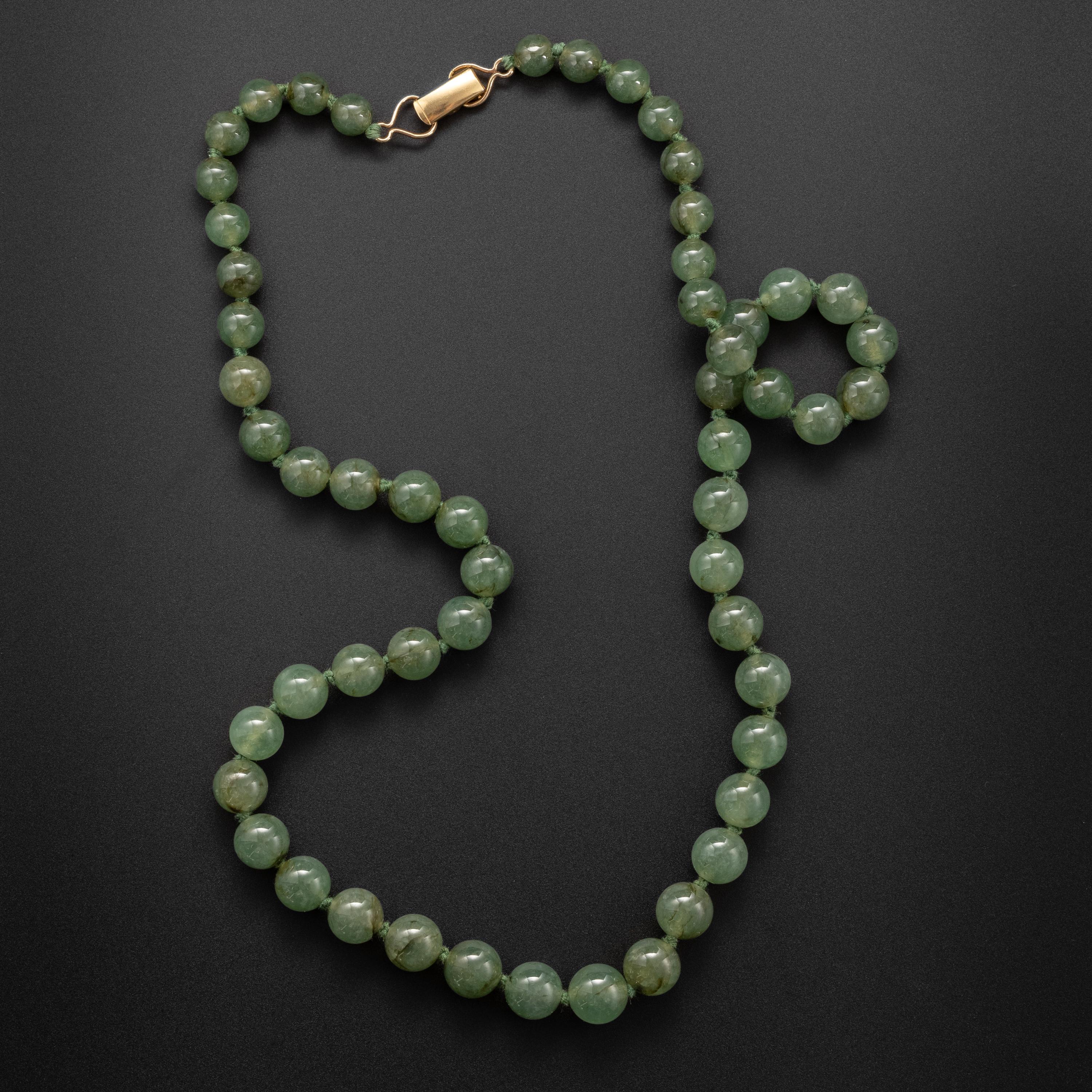 55 succulent, watery light sage green jadeite jade beads have been strung together on sturdy natural cord, knotted between each bead, and finished with a simple clasp in this distinctive, fetching necklace by revered Hawaiian jeweler, Ming's. Though
