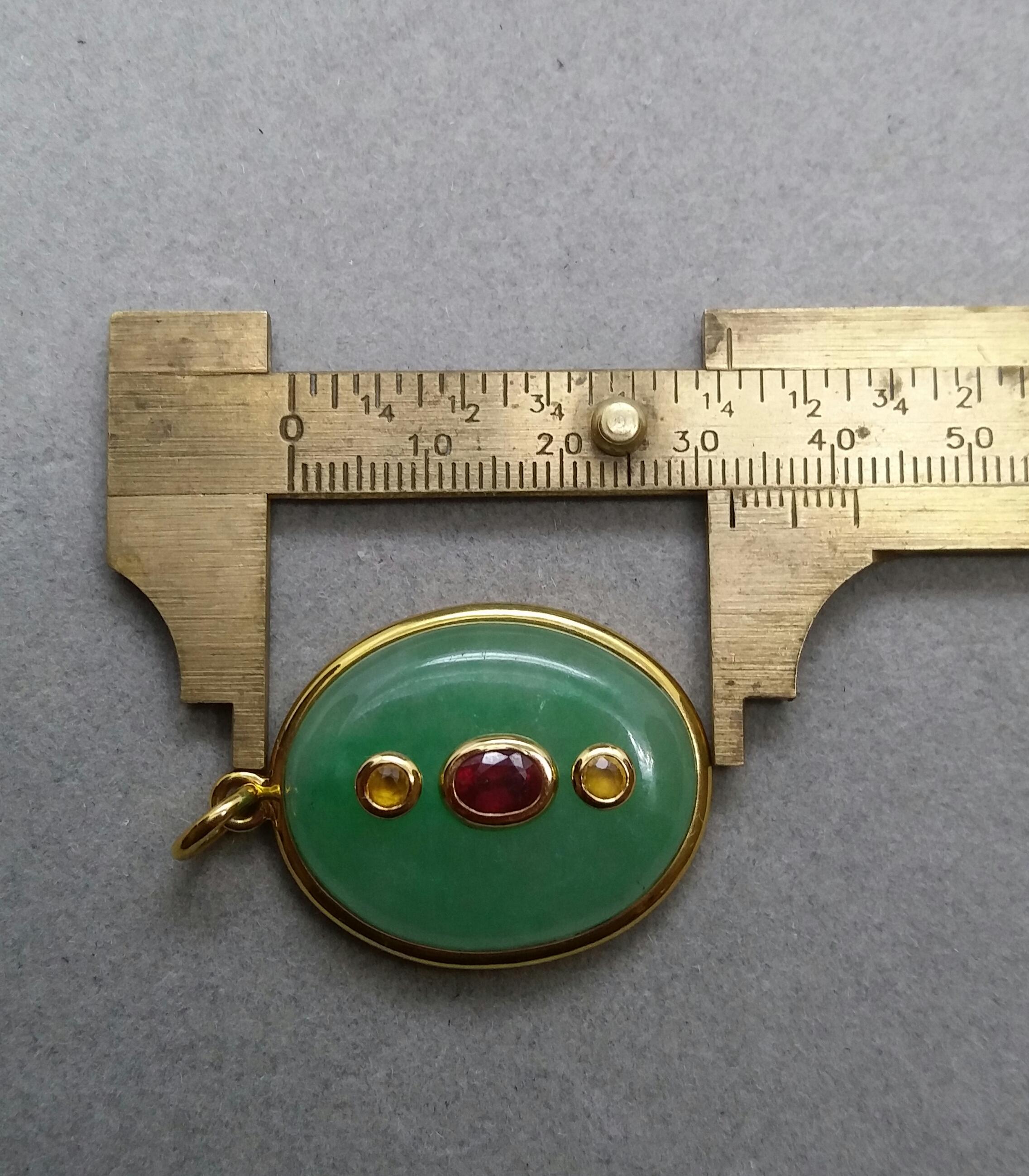 Bigli Cabochon ovale de Jade mesurant 25x32 mm monté en pendentif dans un chaton en or jaune 18kt avec au centre un Rubis ovale à facettes monté en or jaune 18kt.  lunette en or jaune et  2 saphirs jaunes également sertis dans une lunette en or