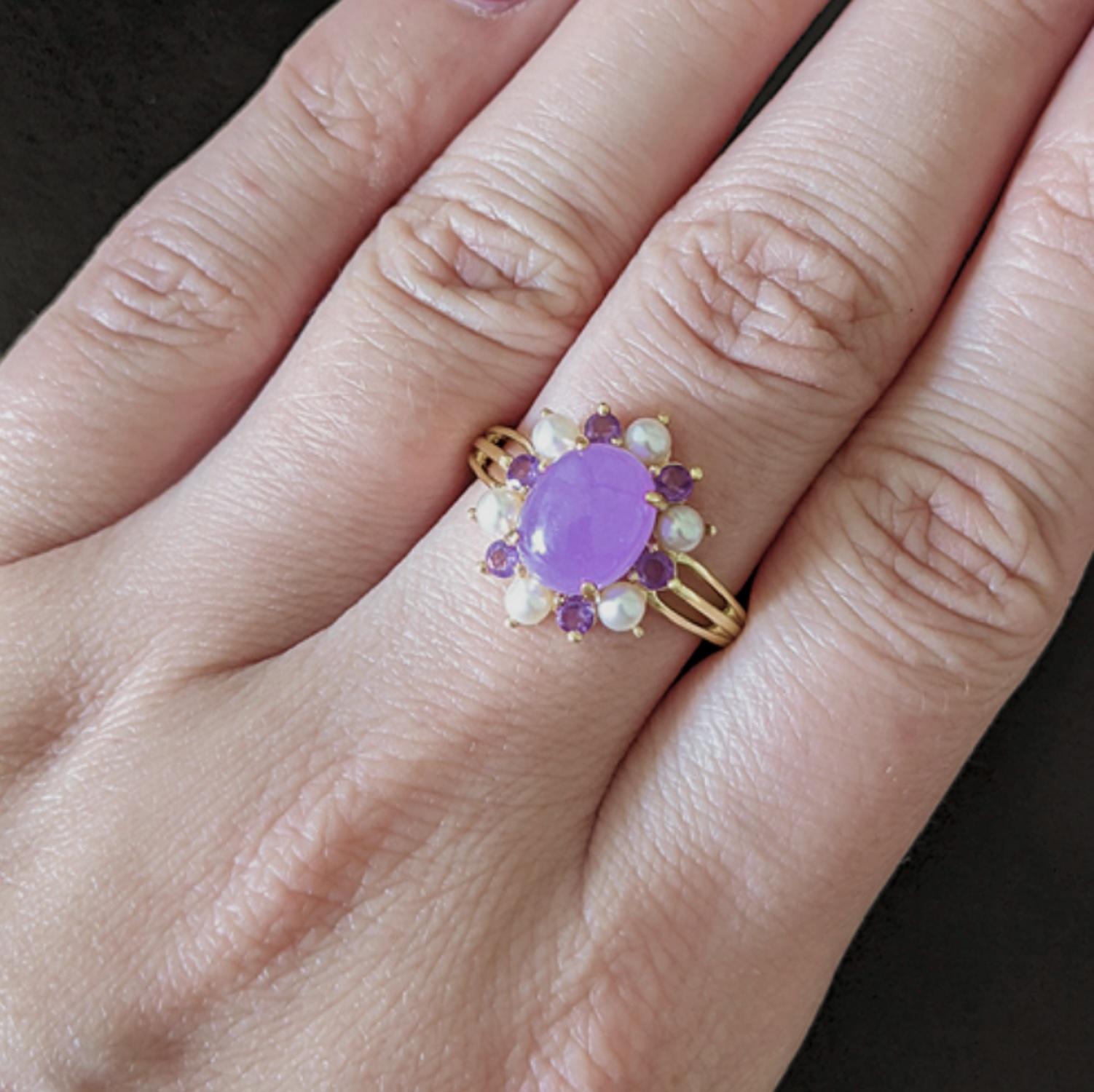 An eye catching lavender jade, amethyst, and pearl cocktail ring offers rich color and a classic design. The jade cabochon is a vibrant purple hue, and it is perfectly set off by a halo of lively amethysts and lustrous pearls. The vivid purple is