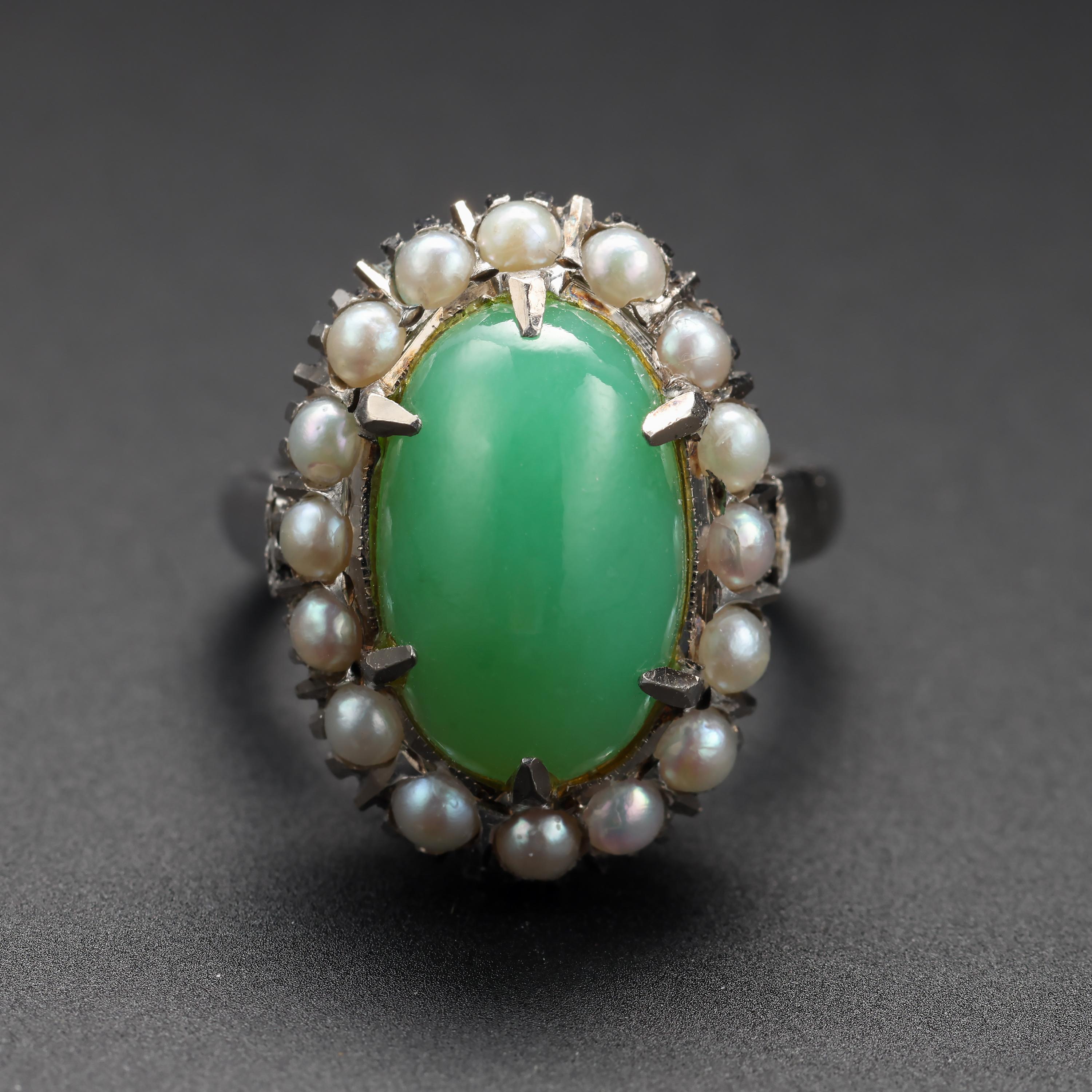 A large oval cabochon of translucent seafoam green jadeite jade is surrounded by 16 luminous natural pearls in this ever-stylish 14K white gold halo ring from the early 1950s.

The jade stone is natural and untreated and displays a high degree of