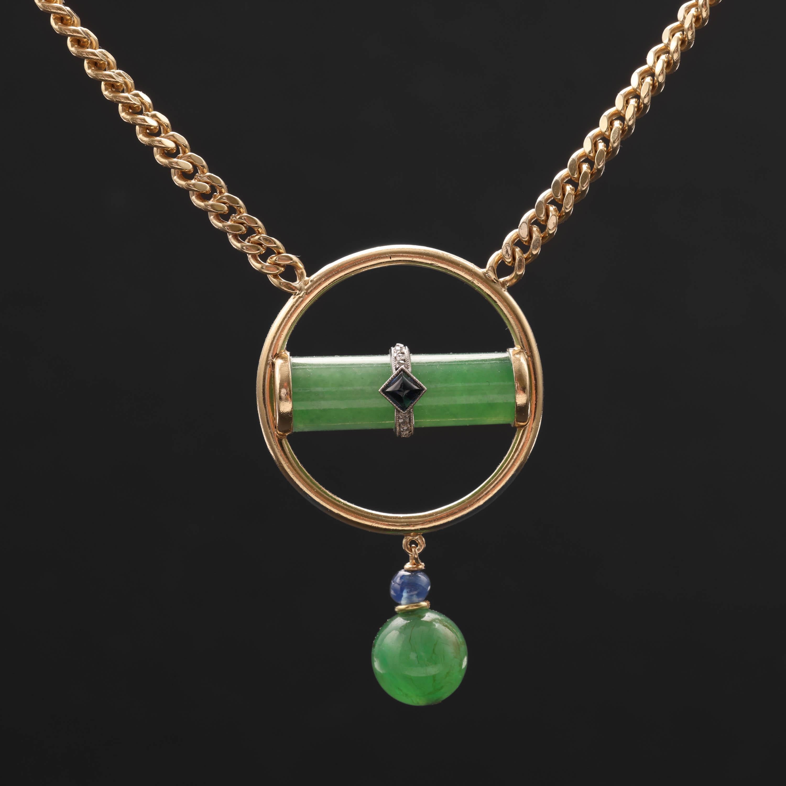 A stunning jade pendant featuring an apple-green cylinder of certified natural and untreated jadeite jade, wrapped in a slender platinum band and set with several tiny white diamonds. A sugarloaf cabochon sapphire is set neatly in the center. A hoop