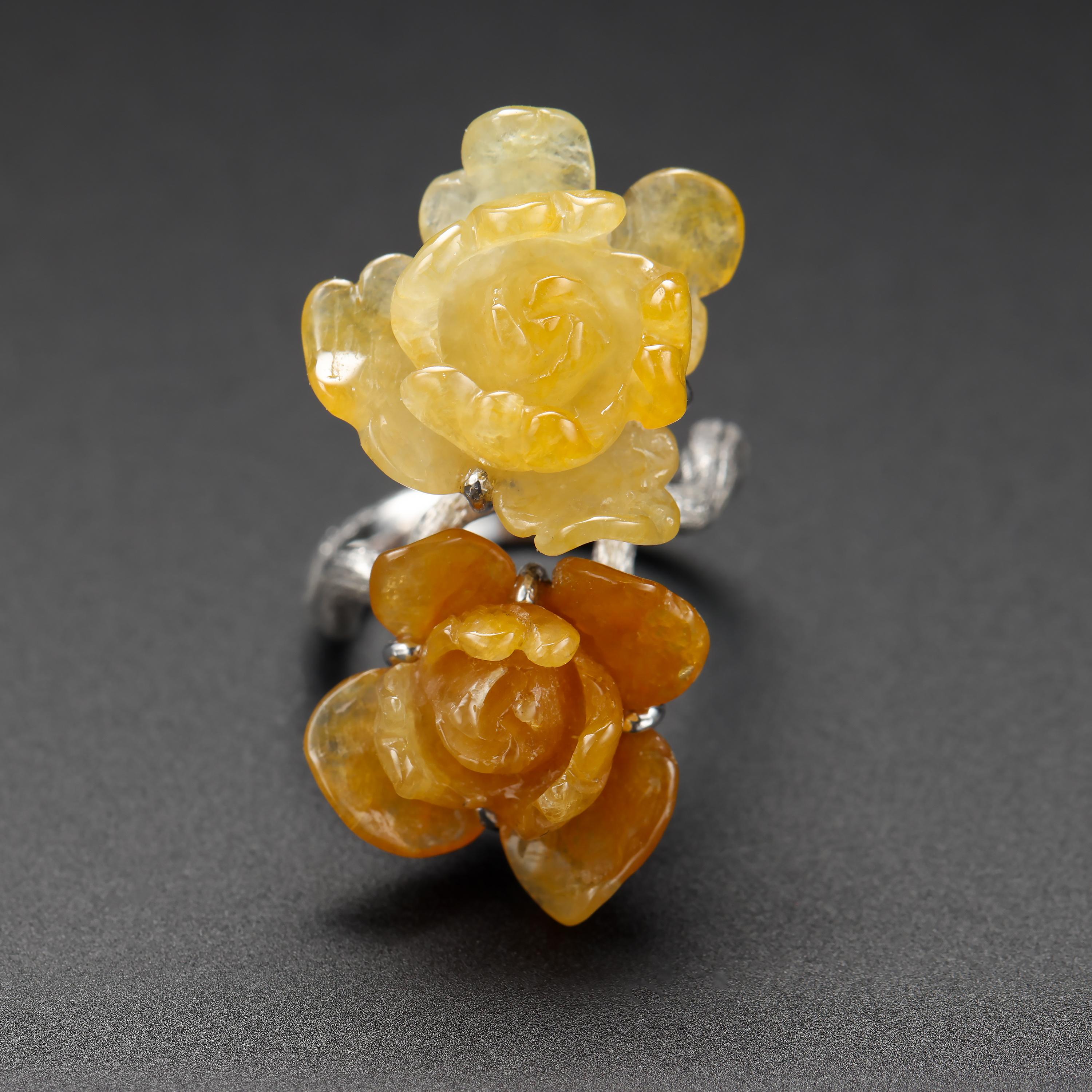 A pair of languid flower blossoms glowing in tropical heat—one orangy-yellow, one lighter yellow, both clearly carved from the same section of stone— are gripped tight by sturdy prongs in a dense, sturdy 18K white gold mounting of cast construction