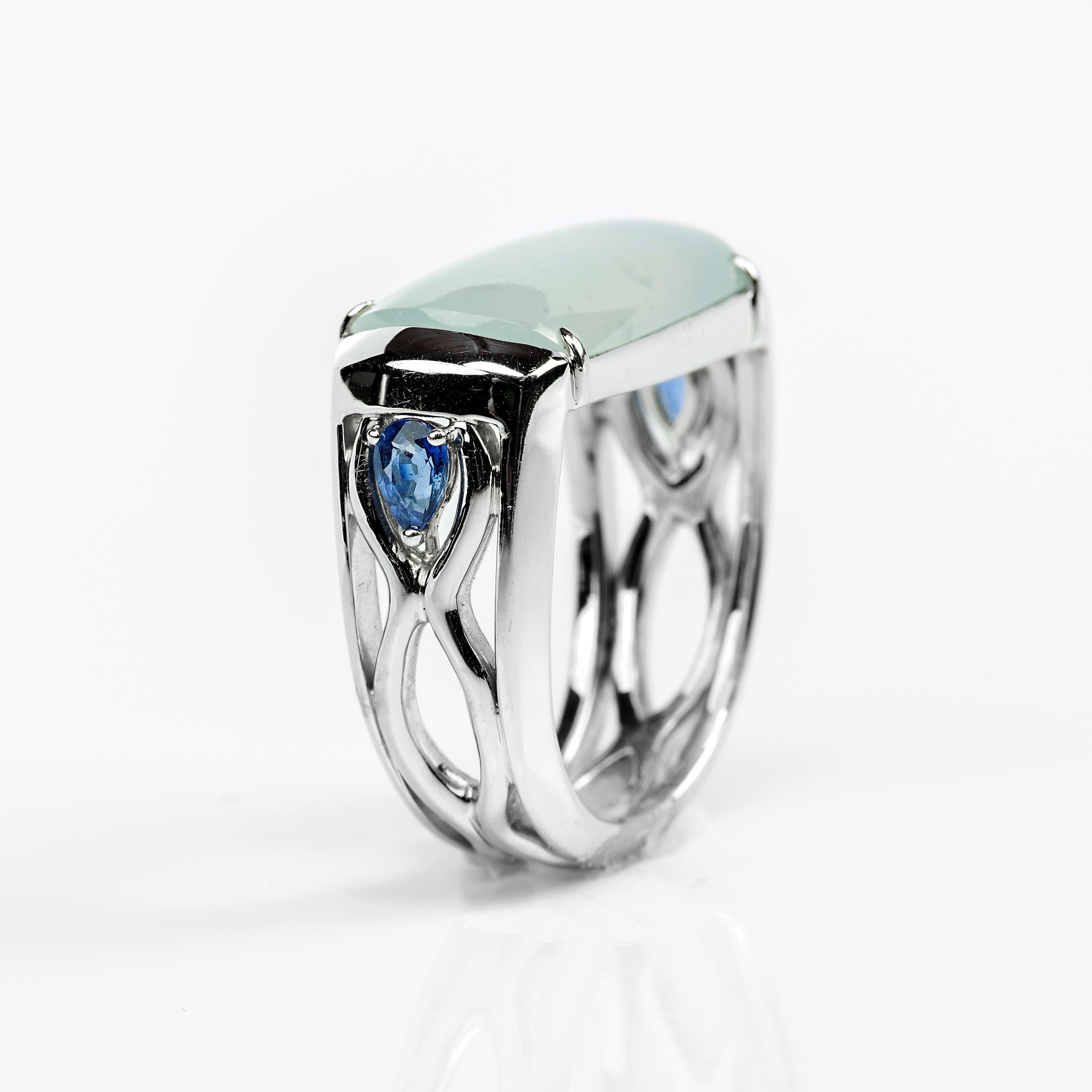 This is a one-of-a-kind hand-fabricated ring of certified untreated Burmese jadeite jade, royal blue sapphires, and 18K white gold. An architectural scaffolding composed of opposing waveforms is set with two pear-shaped approximately .25 carat royal