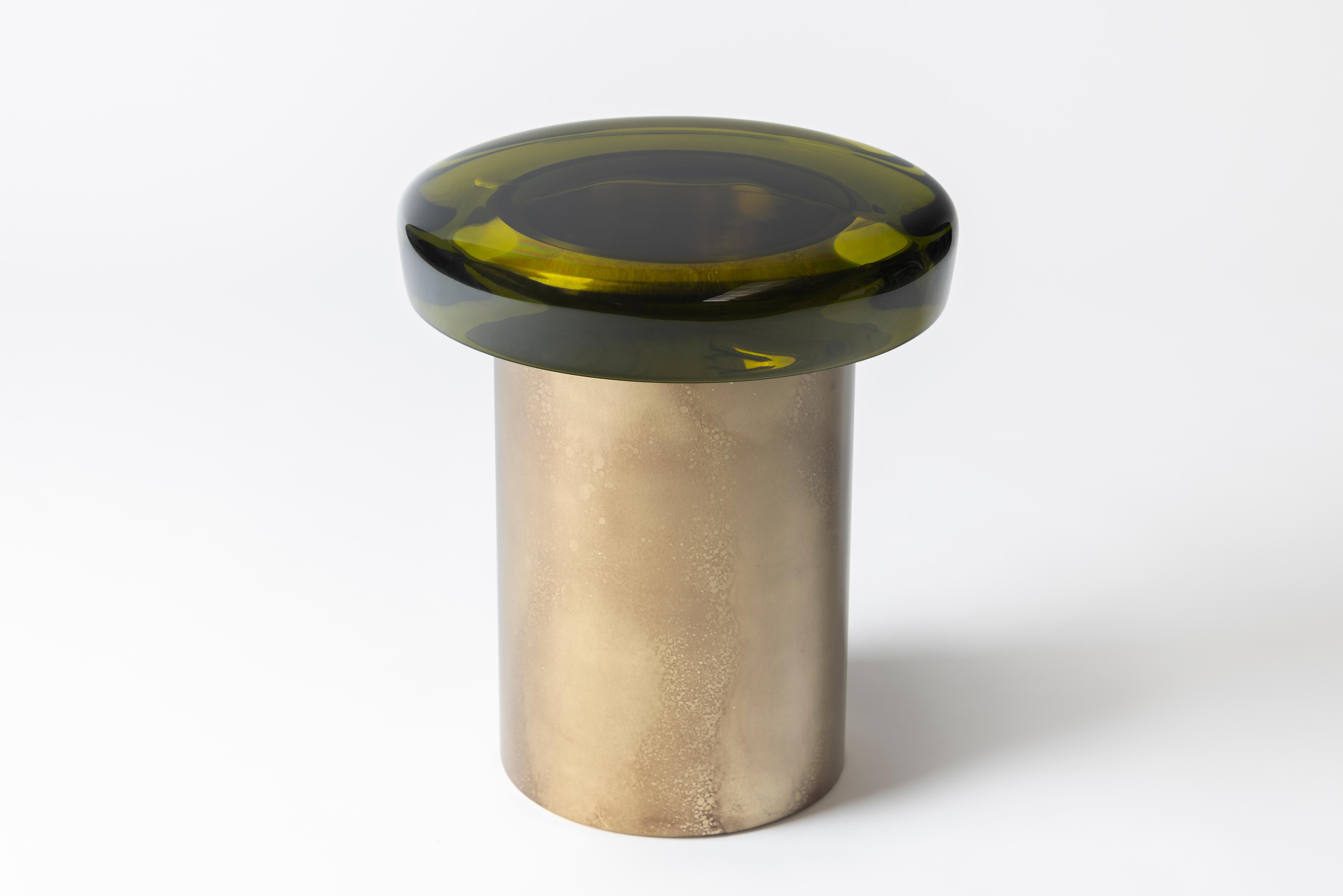 Der Hocker Jade hat eine ätherische Transparenz und eine reflektierende Oberfläche, die auf natürliche Weise mit dem Licht spielt. Die farbenfrohe Sitzfläche ruht auf einem zylindrischen Messingfuß, dessen charakteristische Maserung durch eine