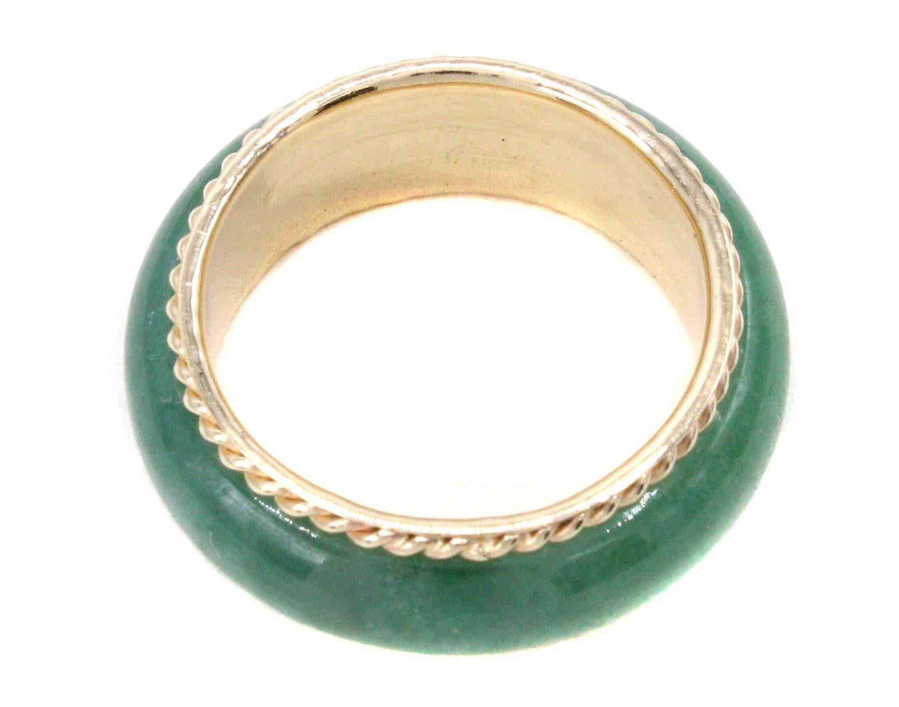 Ring of polished apple green jade cut our of one piece is set in a band of yellow gold embellished by a braided channel on either side. Ring size 6