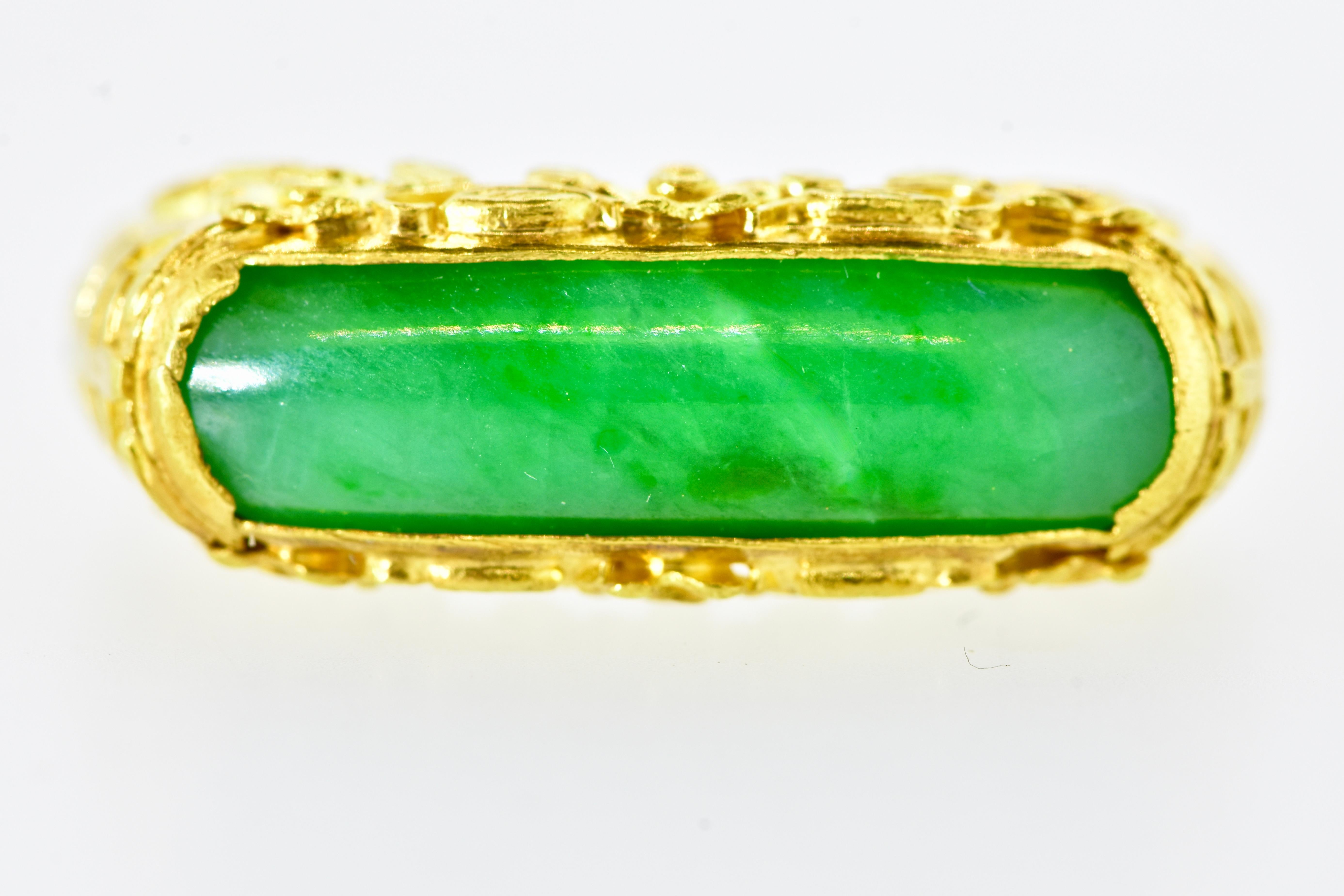 Vintage antique ring centering bright green jadeite jade and decorated, north and south, with a charming floral motif.  This early 20th century ring centers a slightly curved piece of green jadeite jade weighing approximately 3.0 cts. The high karat