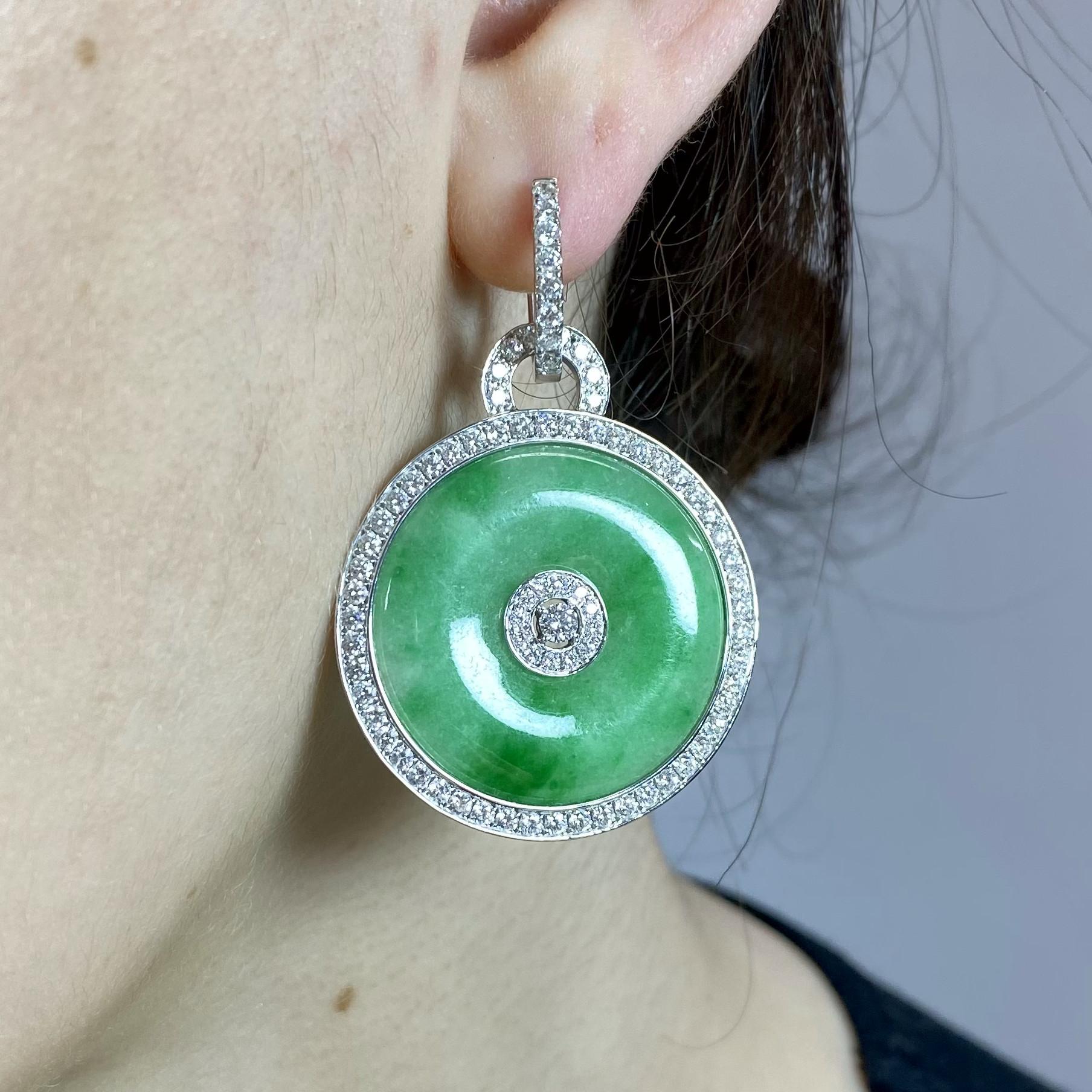 Un paio di moderni orecchini a goccia in giada e diamanti, composti da dischi circolari di giada verde lucida, con un gruppo rotondo di diamanti taglio brillante al centro, ulteriormente circondato da un bordo di diamanti, e da accessori a cerchio