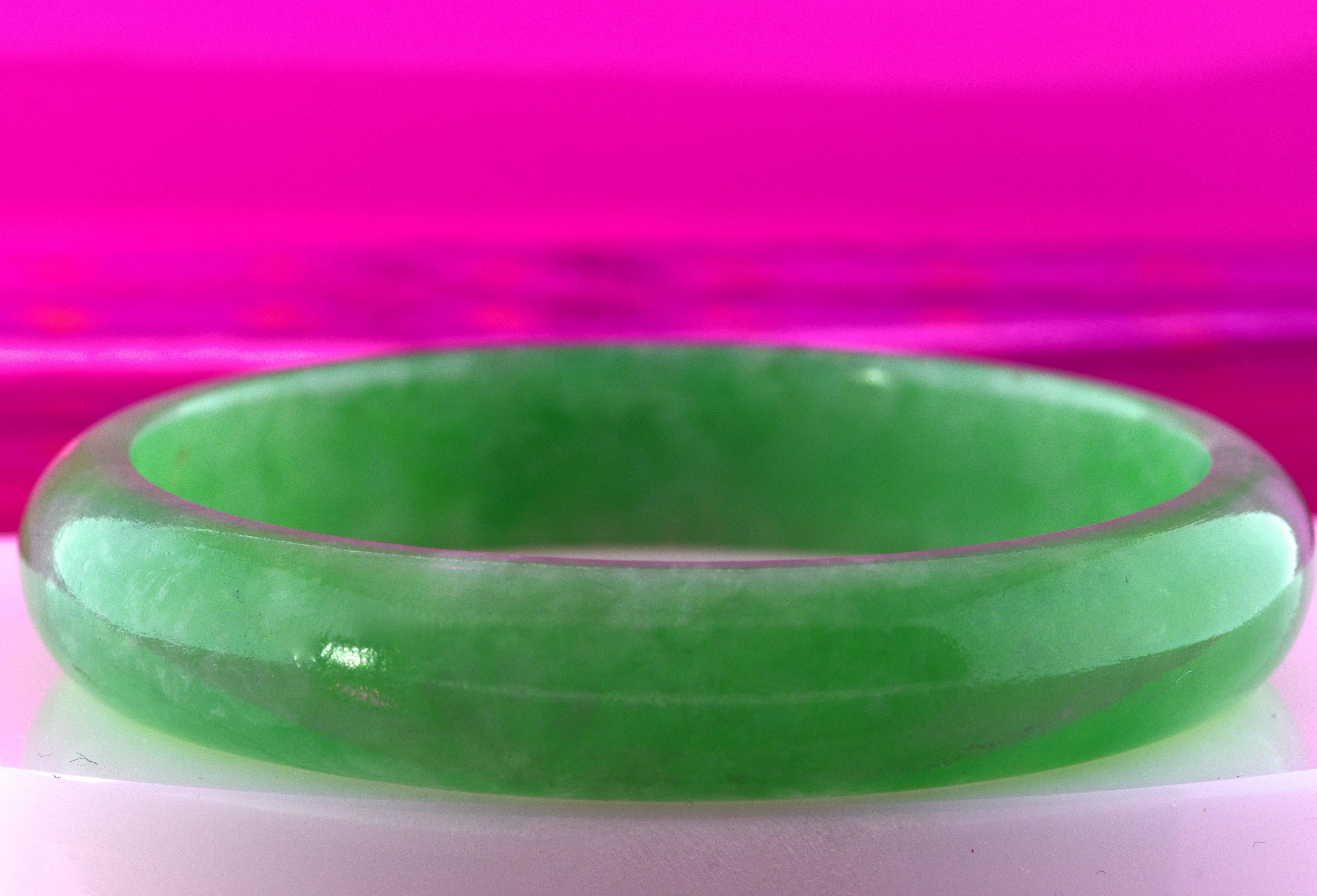 Green jadeite jade - bright and lively carved in to create a bangle bracelet.  This smooth jade piece slips over one's wrist and is a medium size and will fit most wrists.  The jade is 5 mm thick, slightly transparent and slightly mottled from