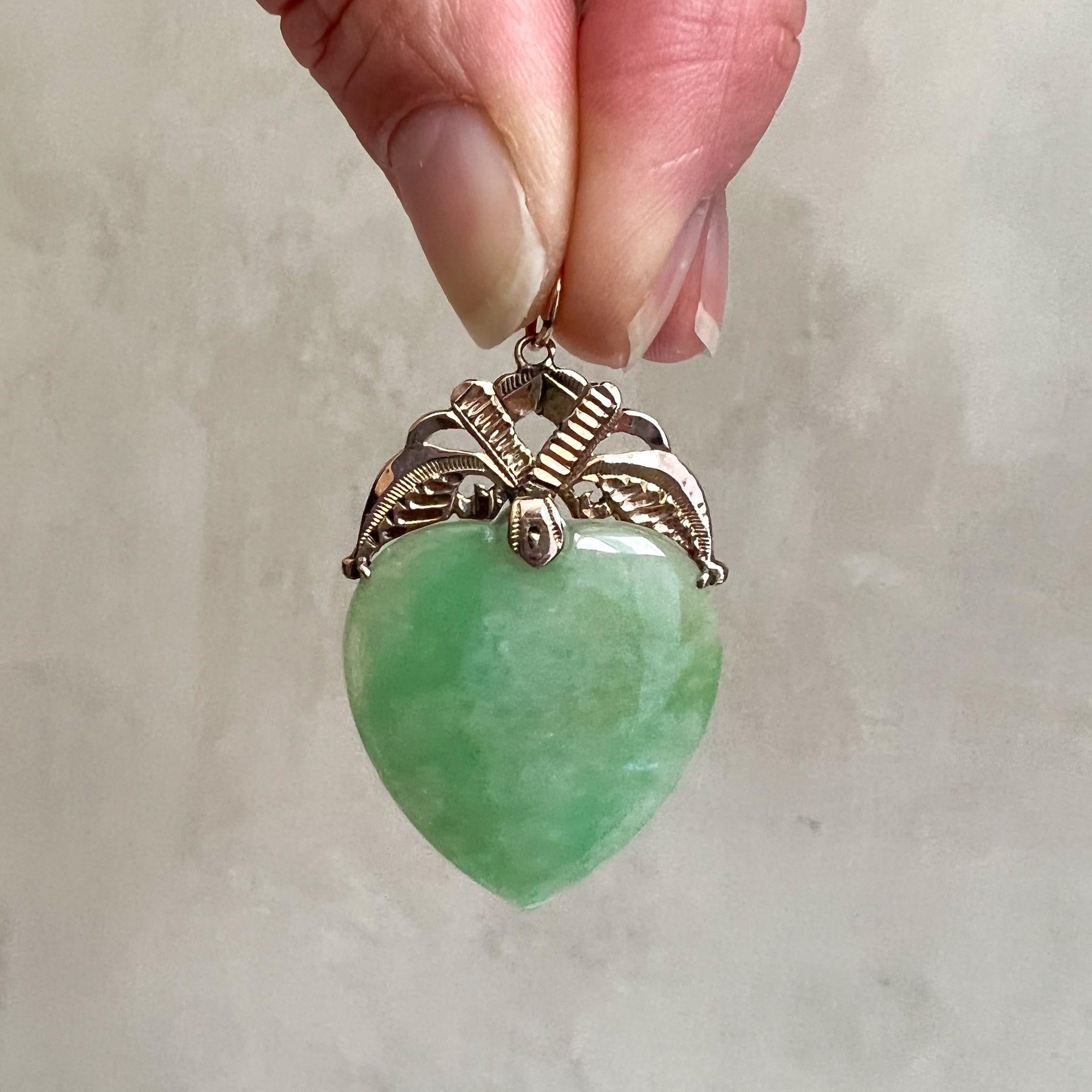 A jadeite jade heart pendant set with a 9 karat gold bail. The jadeite jade has an apple green color, the transparent jade stone is beautifully polished and of high quality. The decorated gold frame above the jade heart is beautifully engraved and