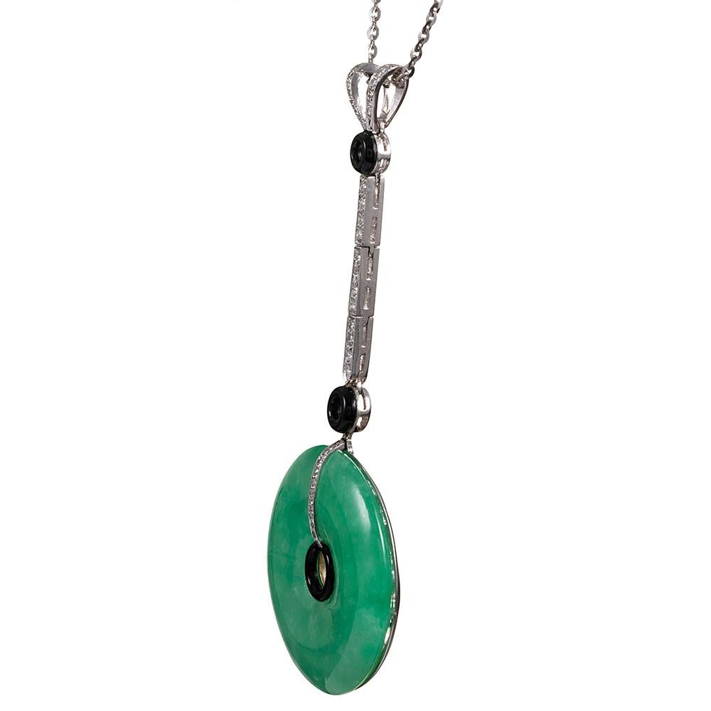 A modern rendering of a glamorous art deco creation, the pendant is made of 18 karat white gold and designed as a jadeite disc, suspended from a diamond-studded matchstick and accented with a split bale and onyx donuts. The piece has a delicate,