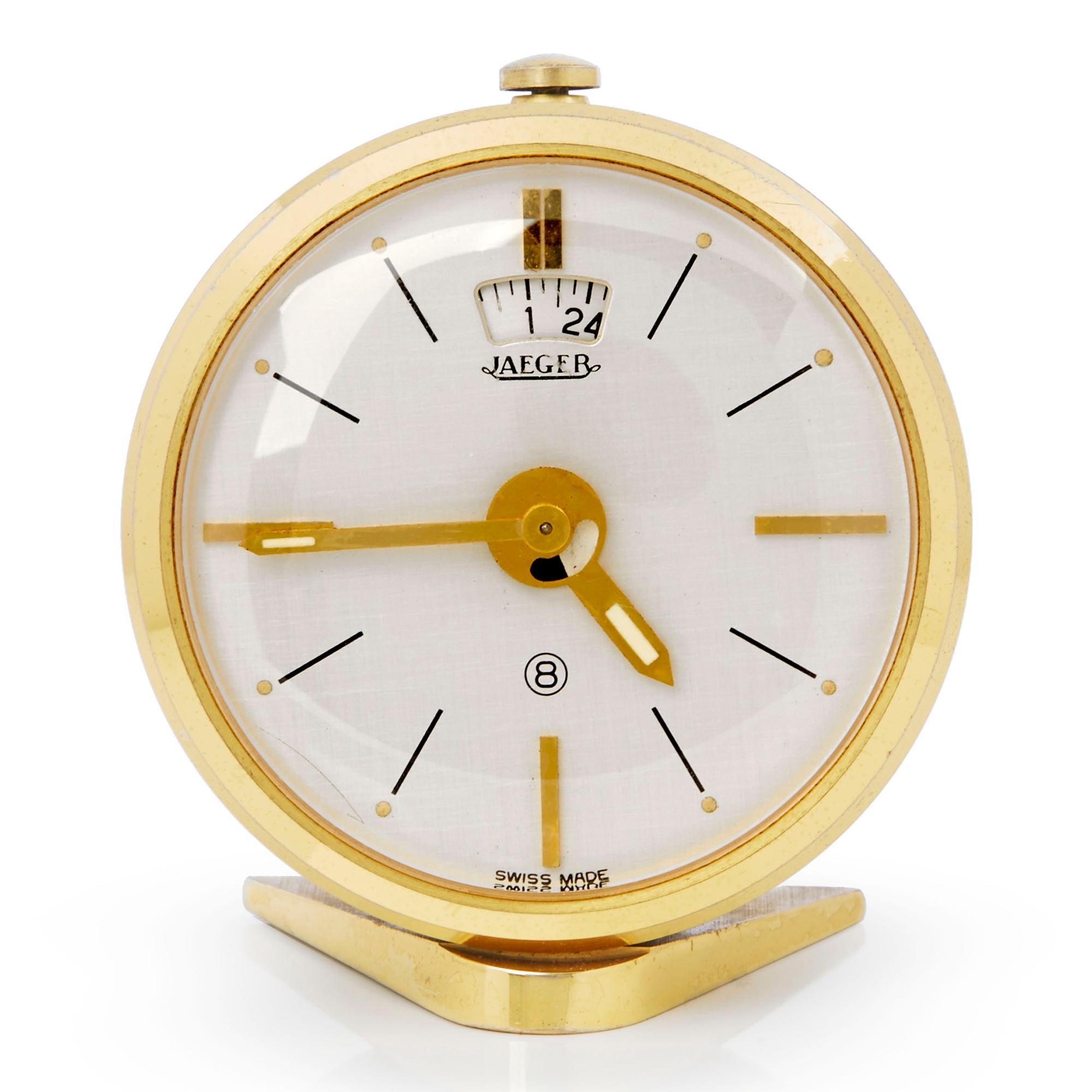 A rare vintage Swiss, Jaeger-LeCoultre 8 day travelling alarm clock, heavily made with with a gold plated brass case with a black enameled casing to the back. The quality clock stands on a 'V' shaped foot and has jewelled watch style Incabloc