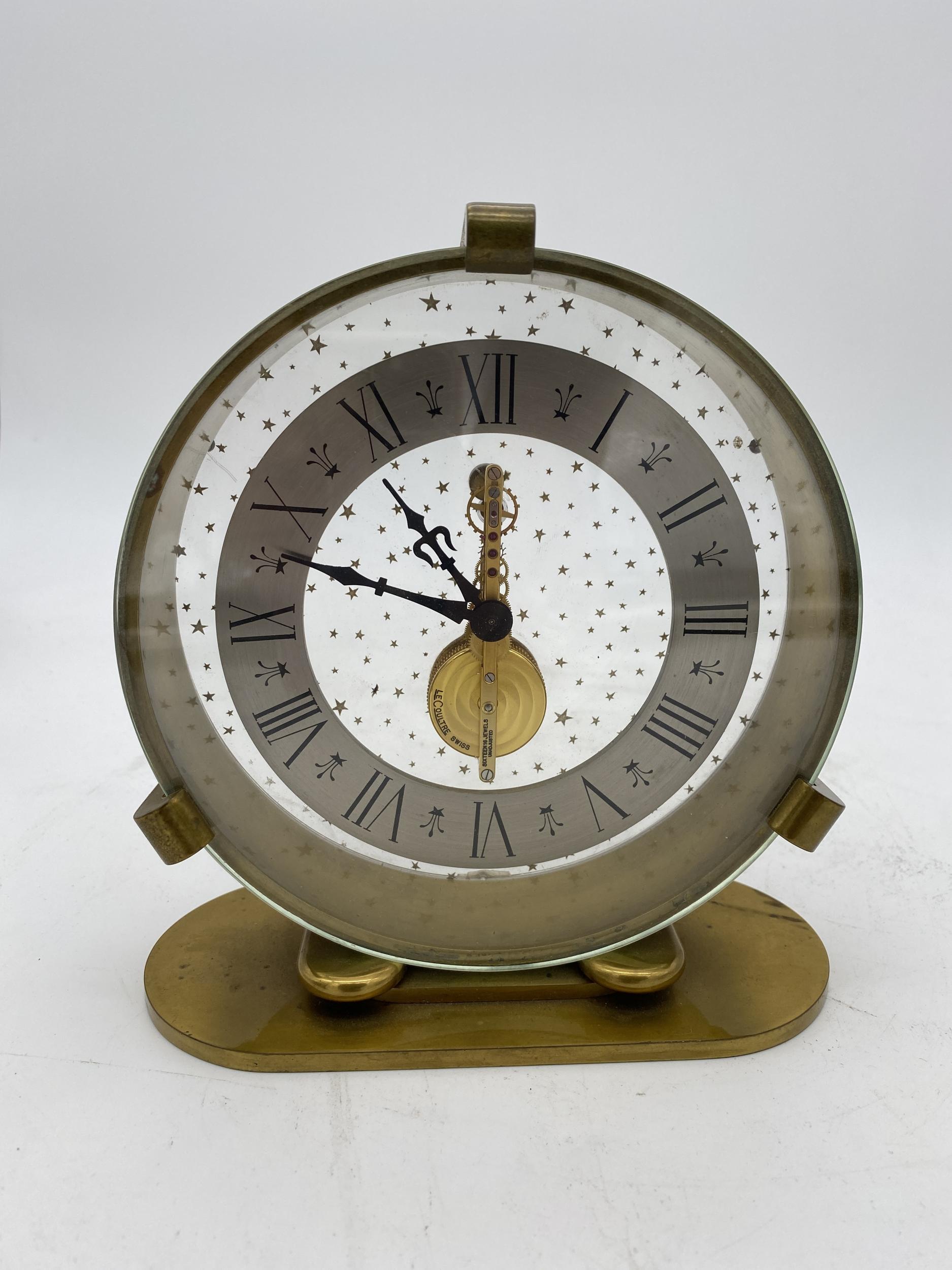 Rare Jaeger LeCoultre 8-day inline movement table desk clock. Attractive case from 1967 in gold color. The clock has two crystals, the back one with stars holds the movement, the front one protects the hands which gives the optical impression of a