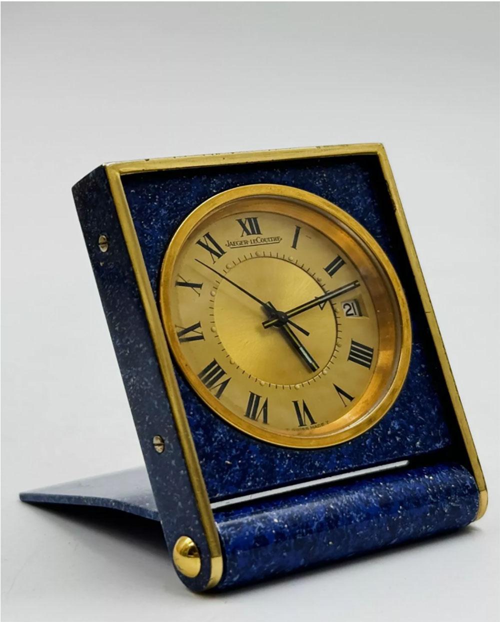 This watch is a vintage classic from the renowned Jaeger-LeCoultre brand, specifically the Mémovox model, an iconic mechanical travel watch from the 1970s.
The watch has a square or rectangular shape, typical of vintage desk clocks. Its design is