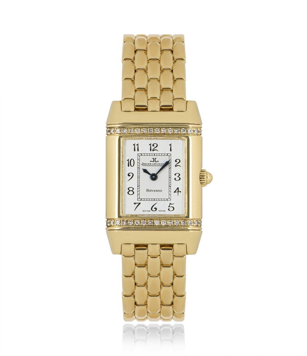 A 21 mm yellow gold Reverso by Jaeger LeCoultre, featuring a silver dial with blued steel hands. The bezel, including the reverse side, is set with a total of approximately 64 round brilliant cut diamonds. A yellow gold bracelet is accompanied by a