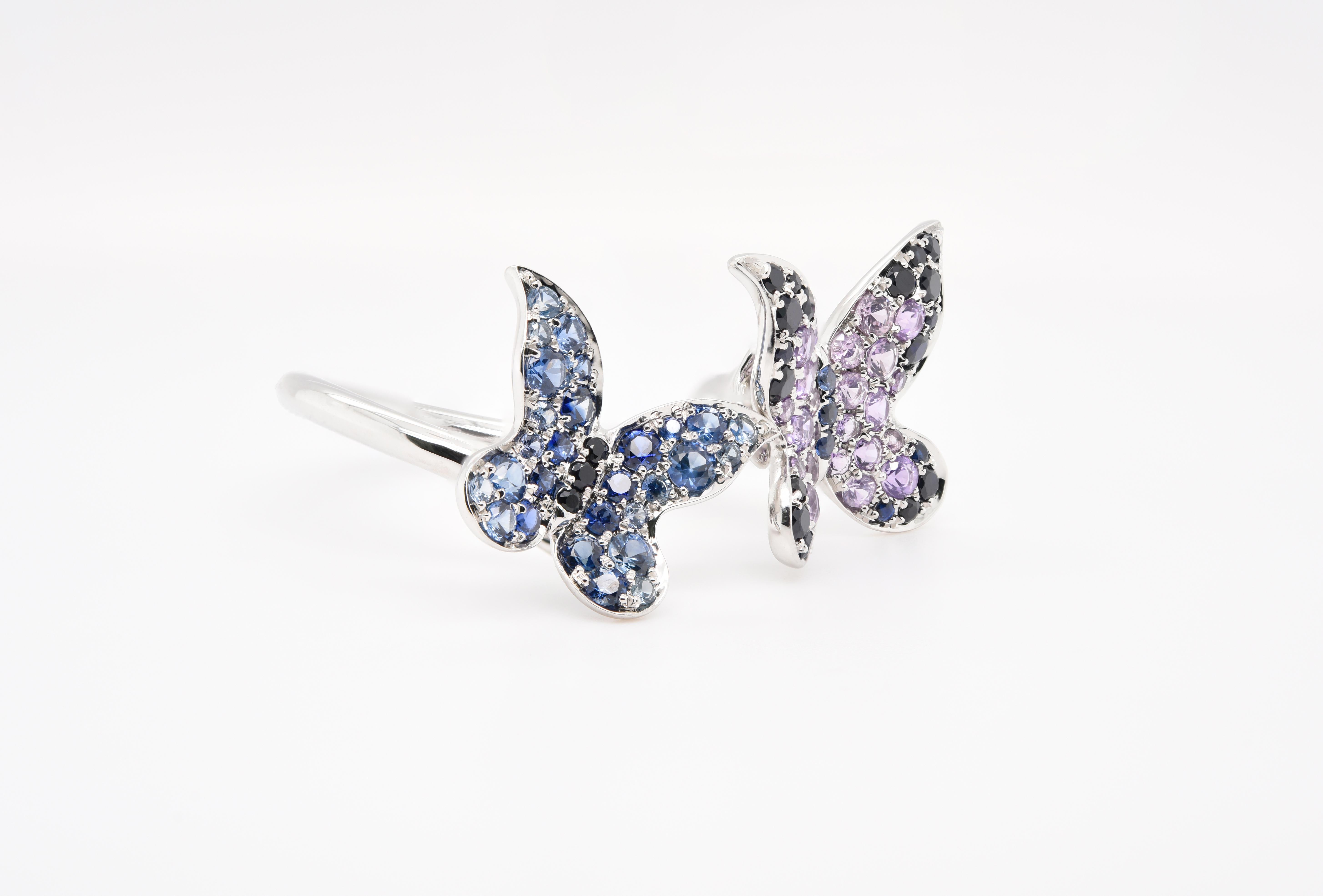 These two butterflies are flying in the air. The butterflies wings are comprised of blue sapphires with black sapphires for its thorax. While the other butterfly wings has purple amethyst and sapphires for its wings with blue sapphires for its