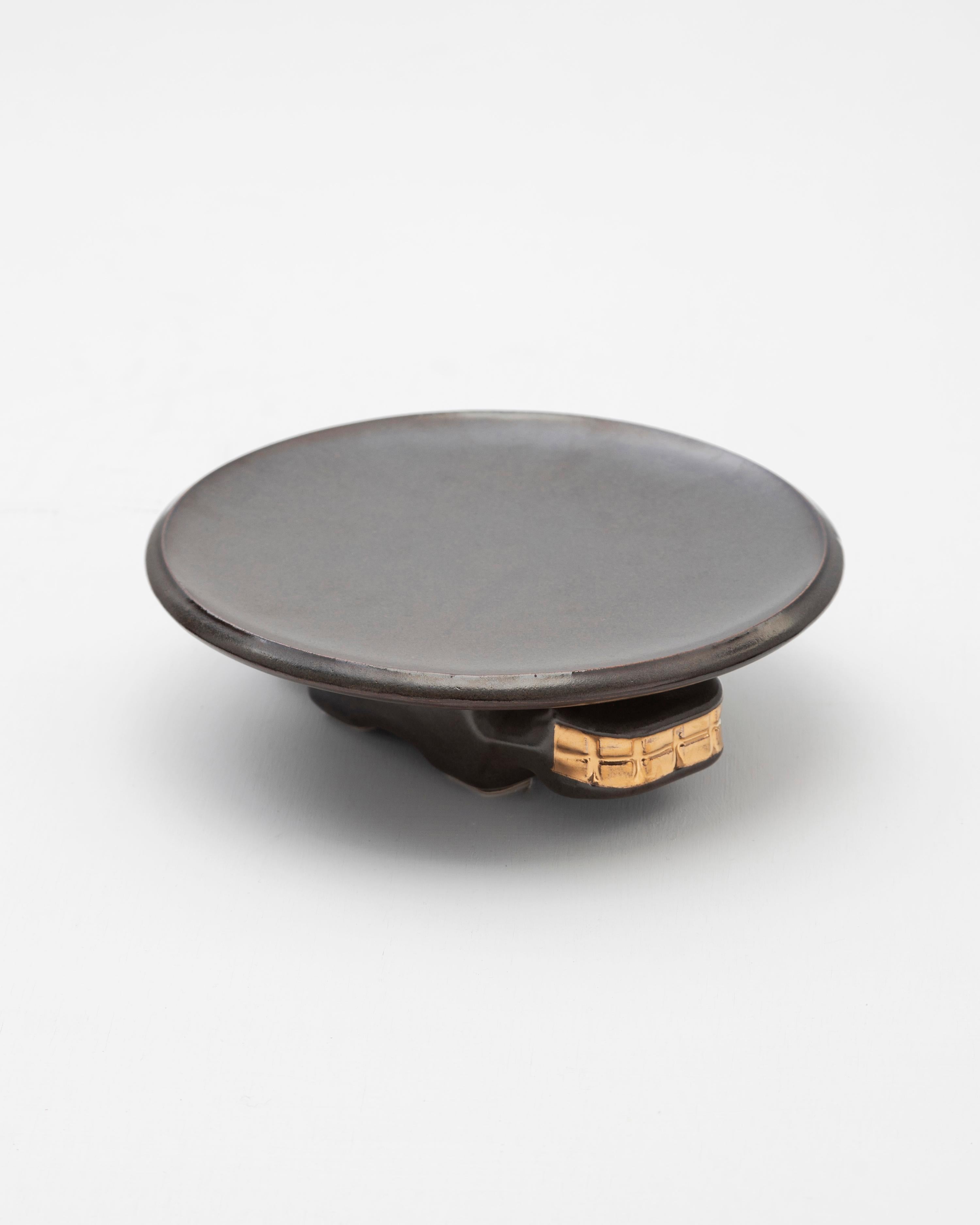 Plato decorativo de cerámica moldeada en barbotina, acabado con un rico esmalte negro o verde oscuro, realzado con detalles de brillo dorado.

Inspirado en el Mortero (Valdivia 4000 - 1800 d.C.), un mortero de piedra tallado a mano con motivos de