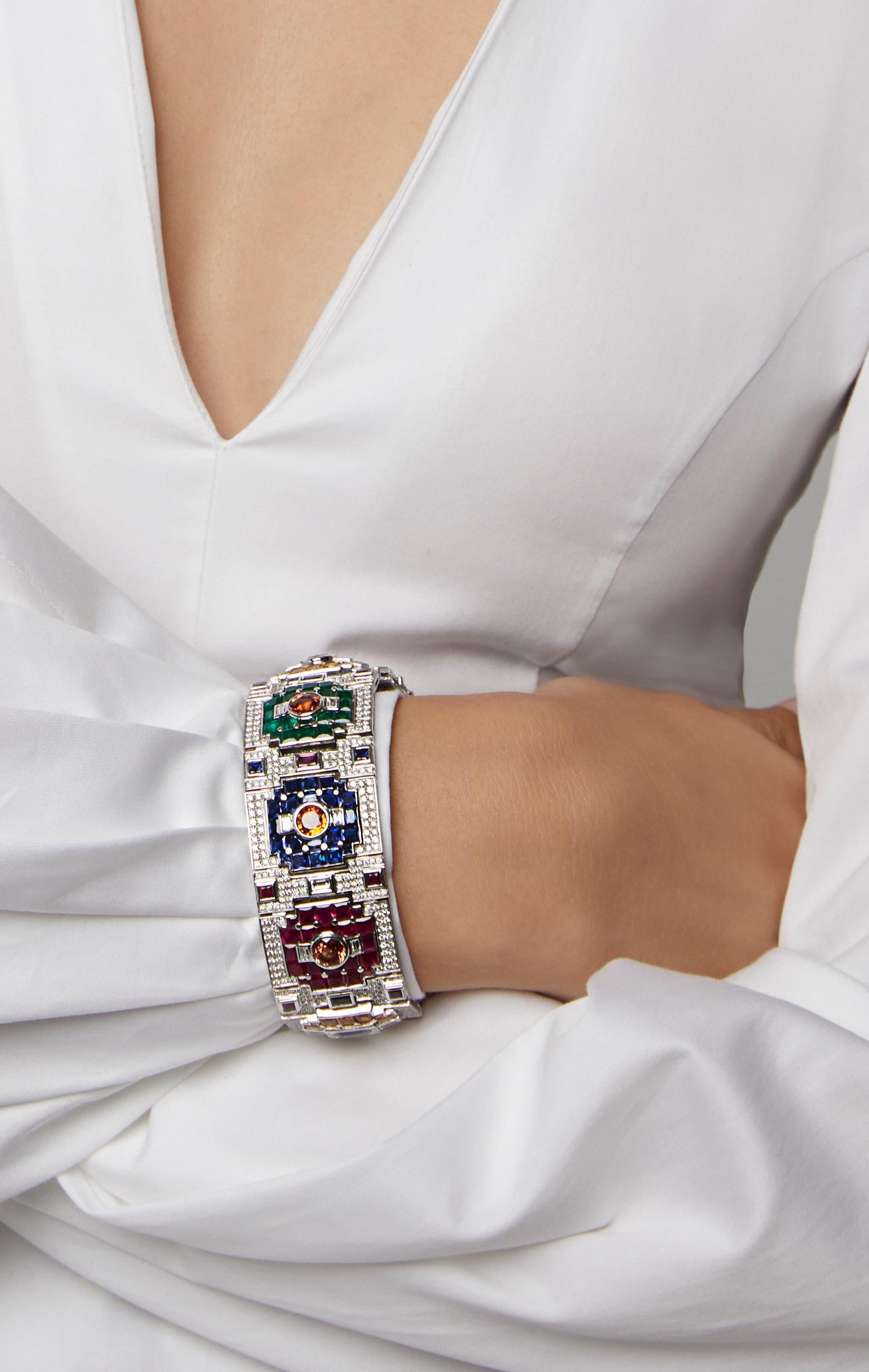 A bracelet by Jahan of geometric panel design set with circular-cut orange sapphire centers between two baguette-cut diamonds within a calibré-cut ruby, emerald, sapphire or yellow sapphire surround in a pavé diamond frame, the central panel set