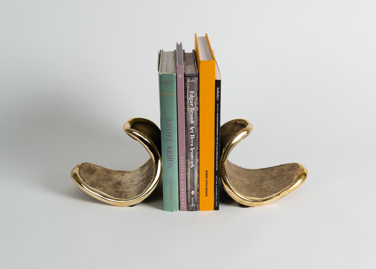 Signed: Jaimal Odedra

Jaimal Odedras’s elegant bookends have rough, textured sides, an edge of polished bronze, and a shape unlikely for their task. They nonetheless perform it admirably, and moreover, create a beautiful splash on either side of