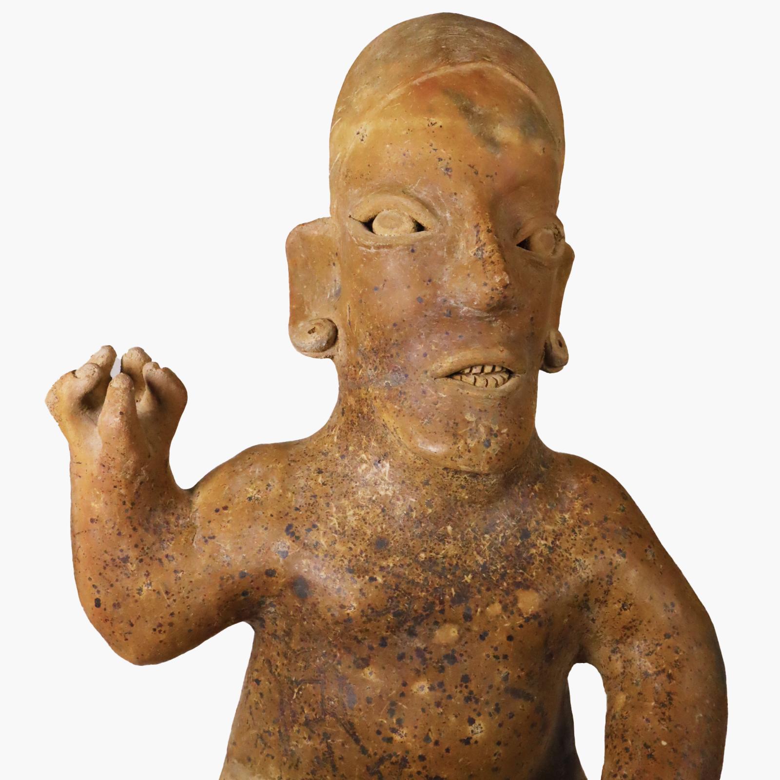 Last chance clearance sale.  Large Jalisco seated figure with raised hand. Fantastic, strong, Picasso-like asymmetric face. The mouth open as if speaking or singing. Large ear spools. Feet and hands carefully sculpted to depict toe and finger nails.