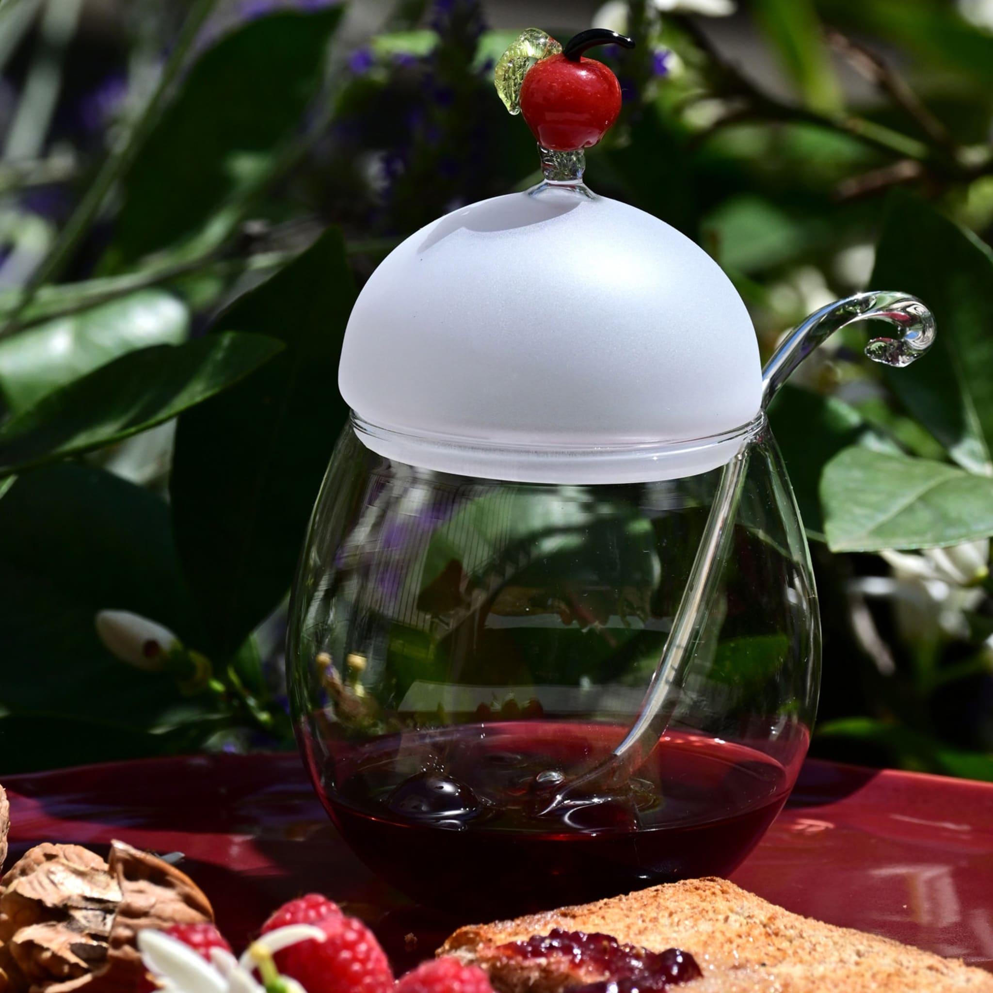 Serve and store jam, confiture, and preserves in this delicate, romantic, granny-style pot with a matching, transparent glass spoon. Its frosted glass cover is topped by a whimsical red apple. It takes two skilled artisans to complete the item.