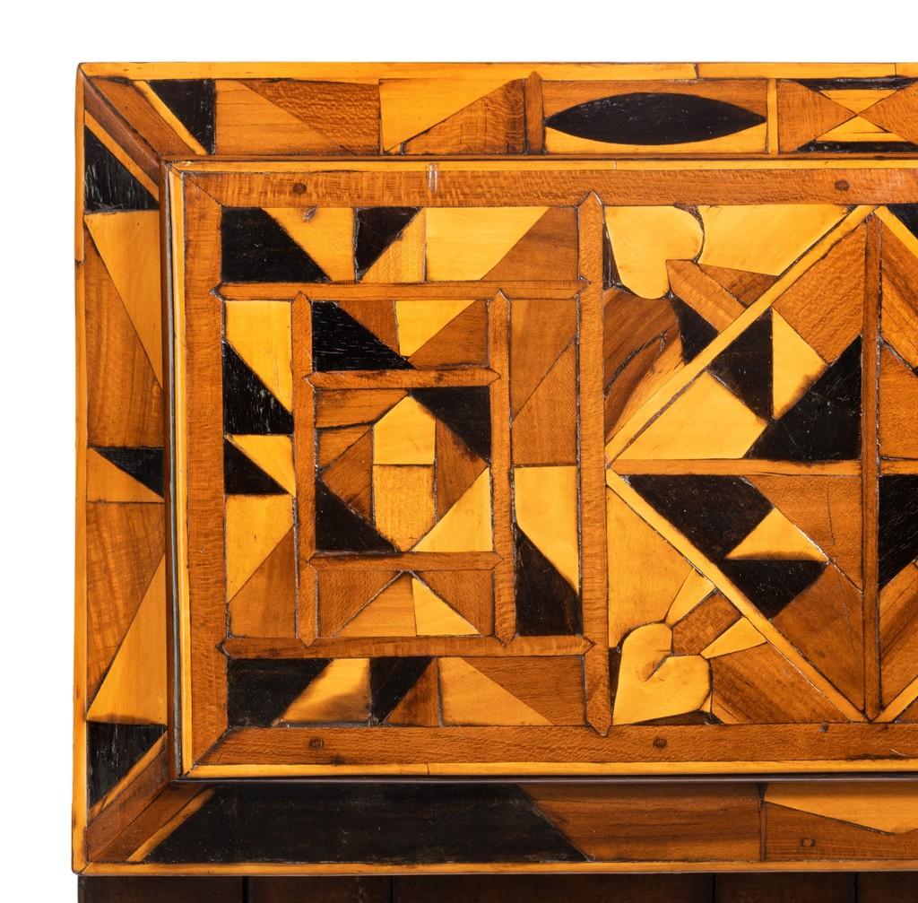 This tea caddy is of rectangular form with a stepped hinged lid, set on bun feet and worked in Caribbean timbers and wooden nails with compass roses and a central starburst roundel on the front, the sides and lid with diamonds, triangles and four