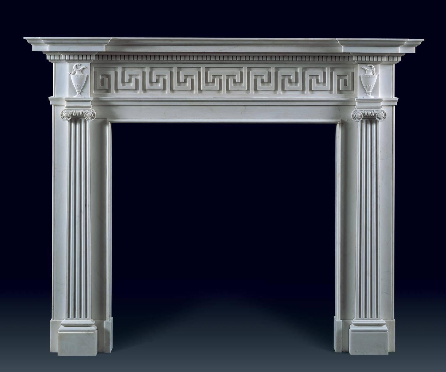 The dramatic classical proportions and finely carved decoration on this chimneypiece include elegantly fluted Roman ionic pilasters. The key fret carved frieze and the classical urns beneath the dentil moulding on each side reinforce the art of