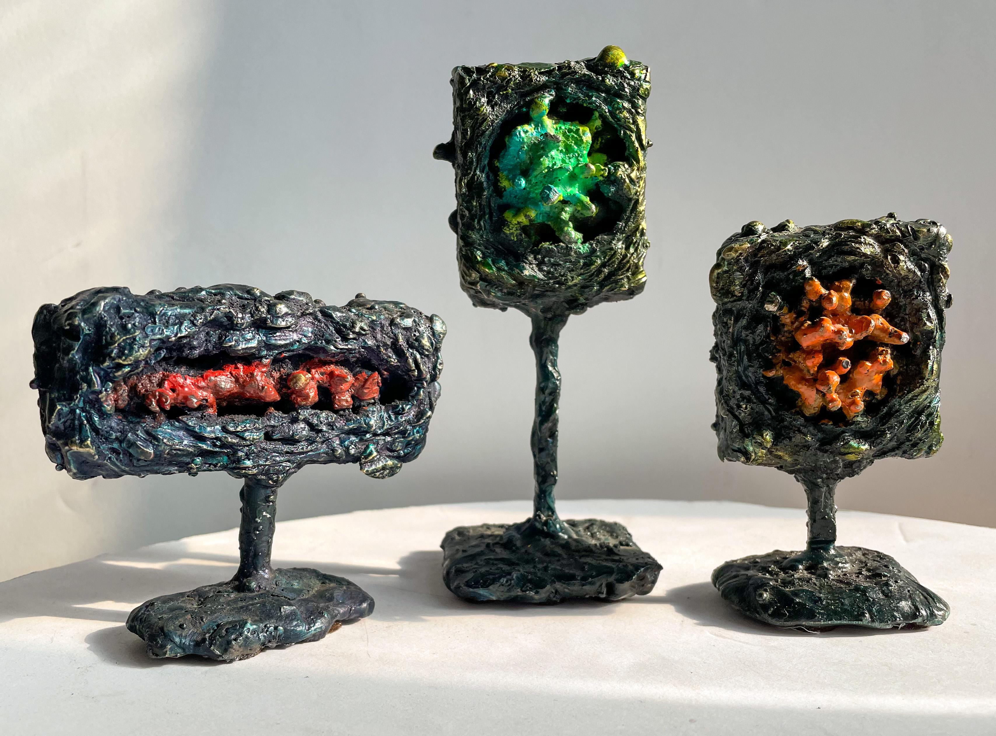 Group of three small abstract sculptures, titled Module Trio, of blackened steel, fused and dyed bronze, and glass enamel. Made in 2019 by American artist James Bearden. The three sculptures, each with a different brightly colored, molten-looking