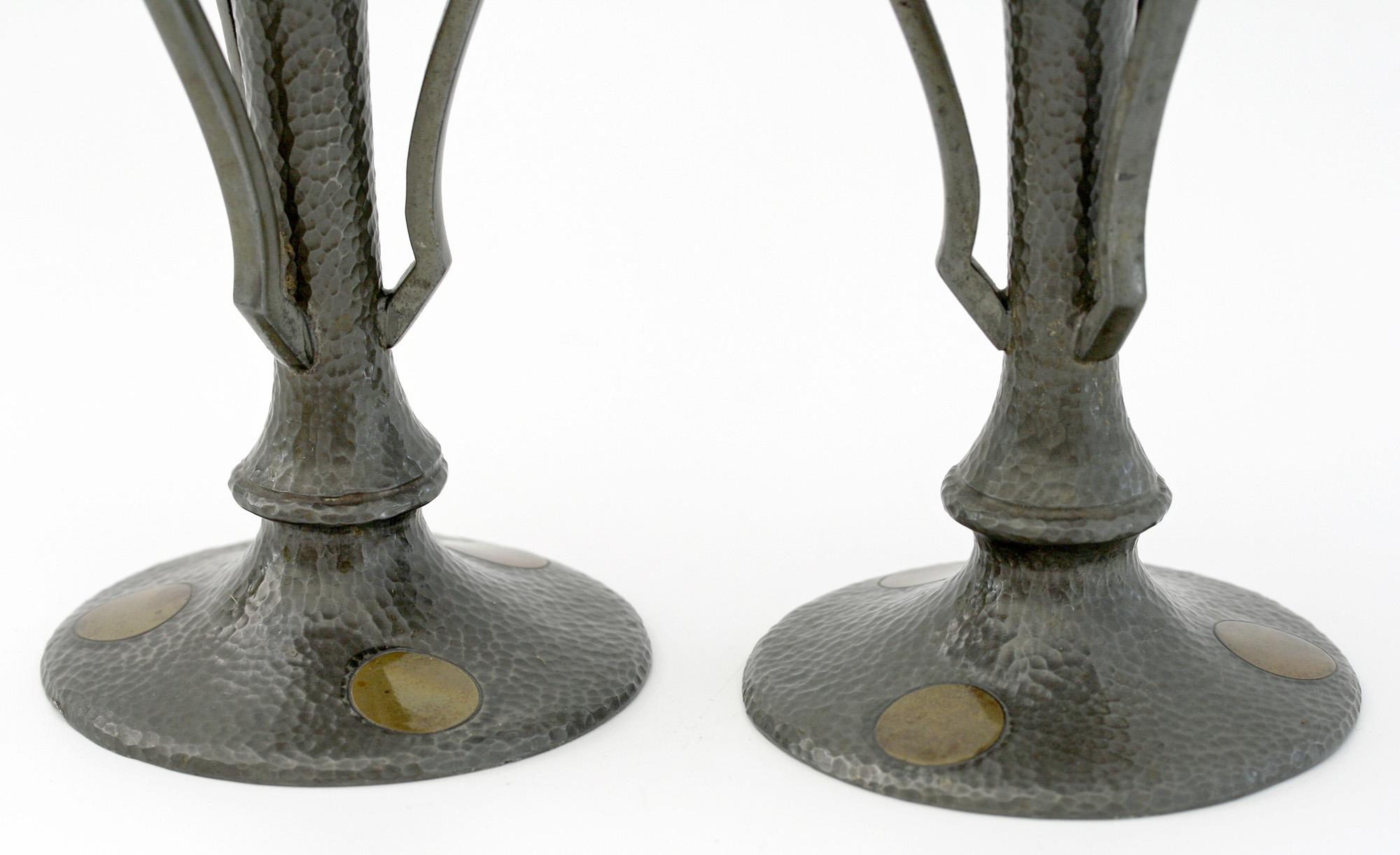 A stylish pair Arts & Crafts pewter candlesticks inset with brass decoration by James Dixon & Sons, Sheffield and dating from circa 1890. The pewter vases stand on a wide rounded base the stem applied with three angled handles and supporting a