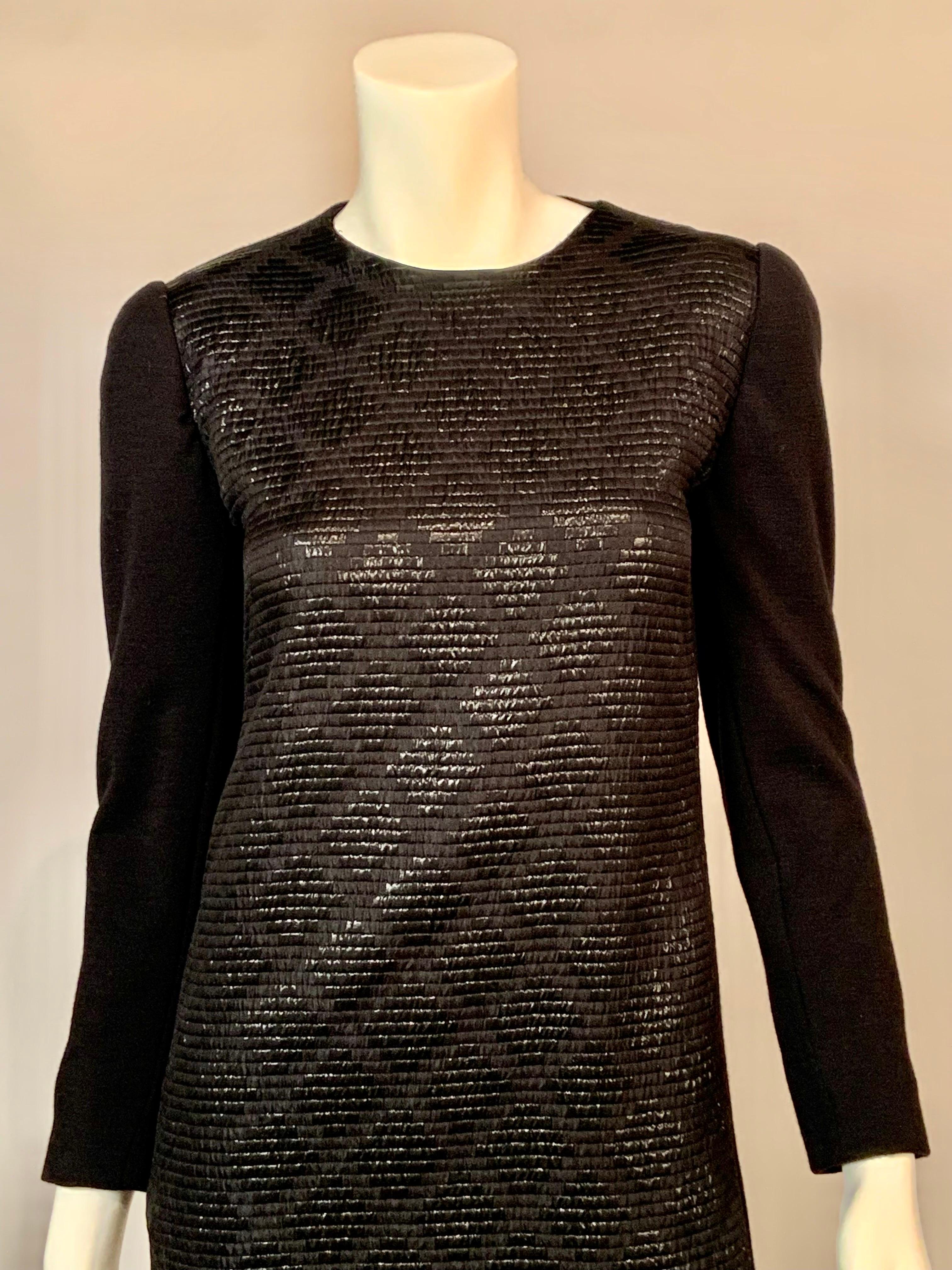 James Galanos a conçu une robe noire élégante en utilisant deux tissus différents pour plus d'intérêt.  Le devant de la robe est en soie côtelée avec un motif métallique en forme de diamant. Le corps de la robe est un jersey de laine noir.  La robe