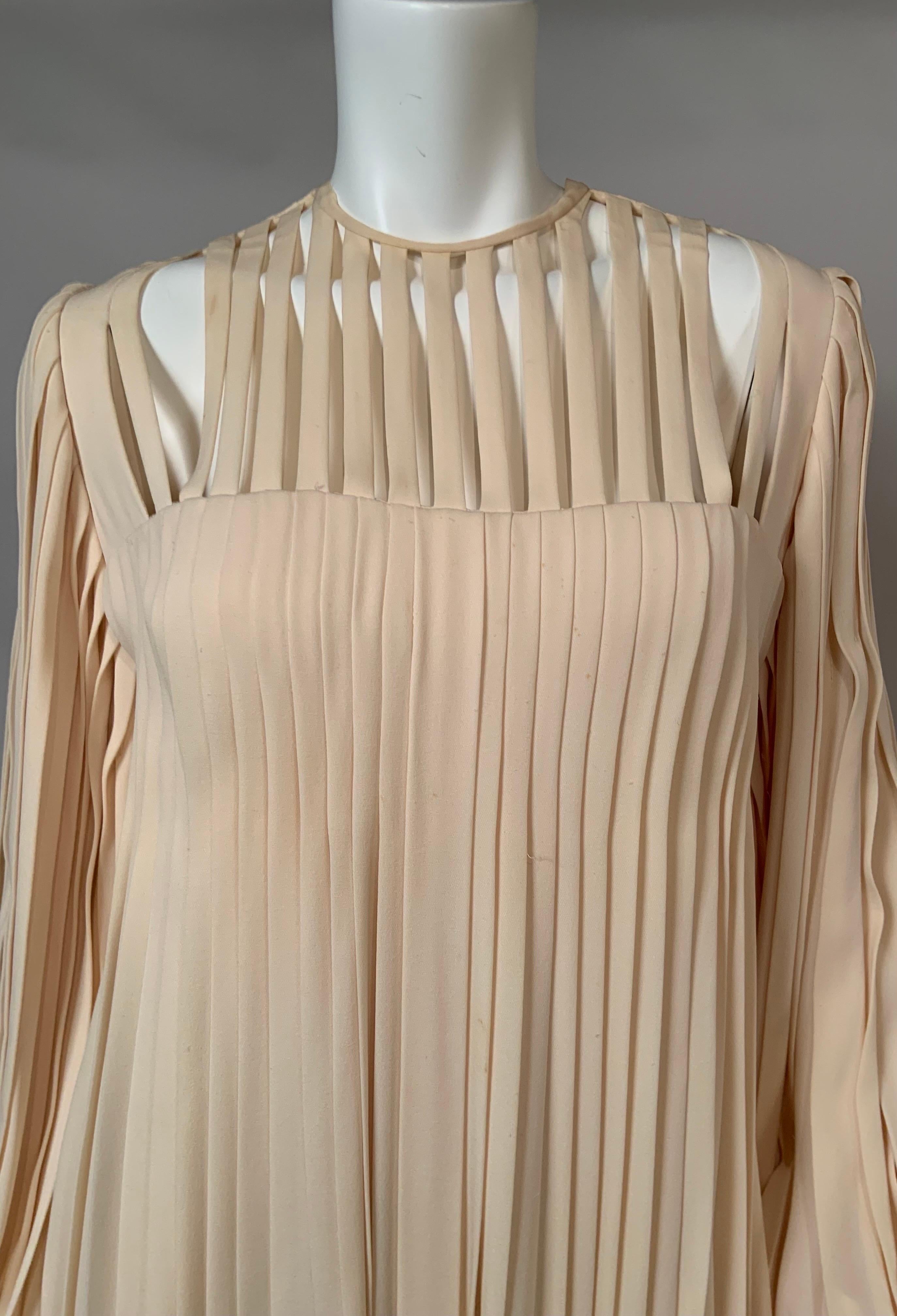 James Galanos designed this unusual pleated dress using ivory silk crepe. The dress has a very interesting bodice with evenly spaced bands of the fabric revealing the skin of the wearer above a pleated dress.  The long sleeves are fully pleated and