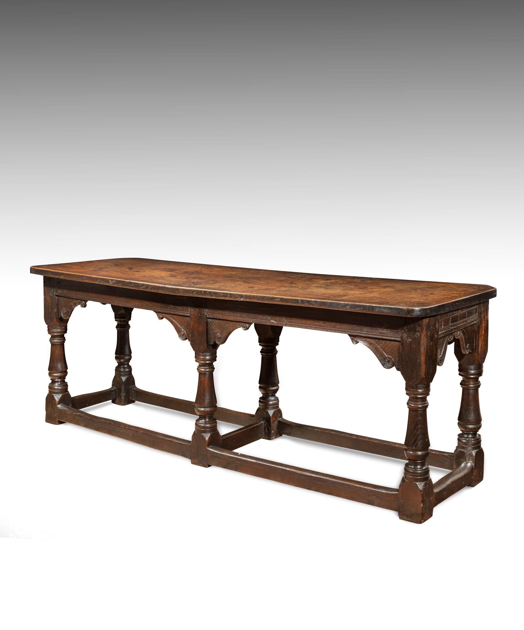 A rare James I carved oak six-leg refectory table; the later one piece Georgian top above a crisply carved frieze with bold S scroll brackets and raised on six turned legs united by stretchers. The tabletop has a wonderful color and patination and