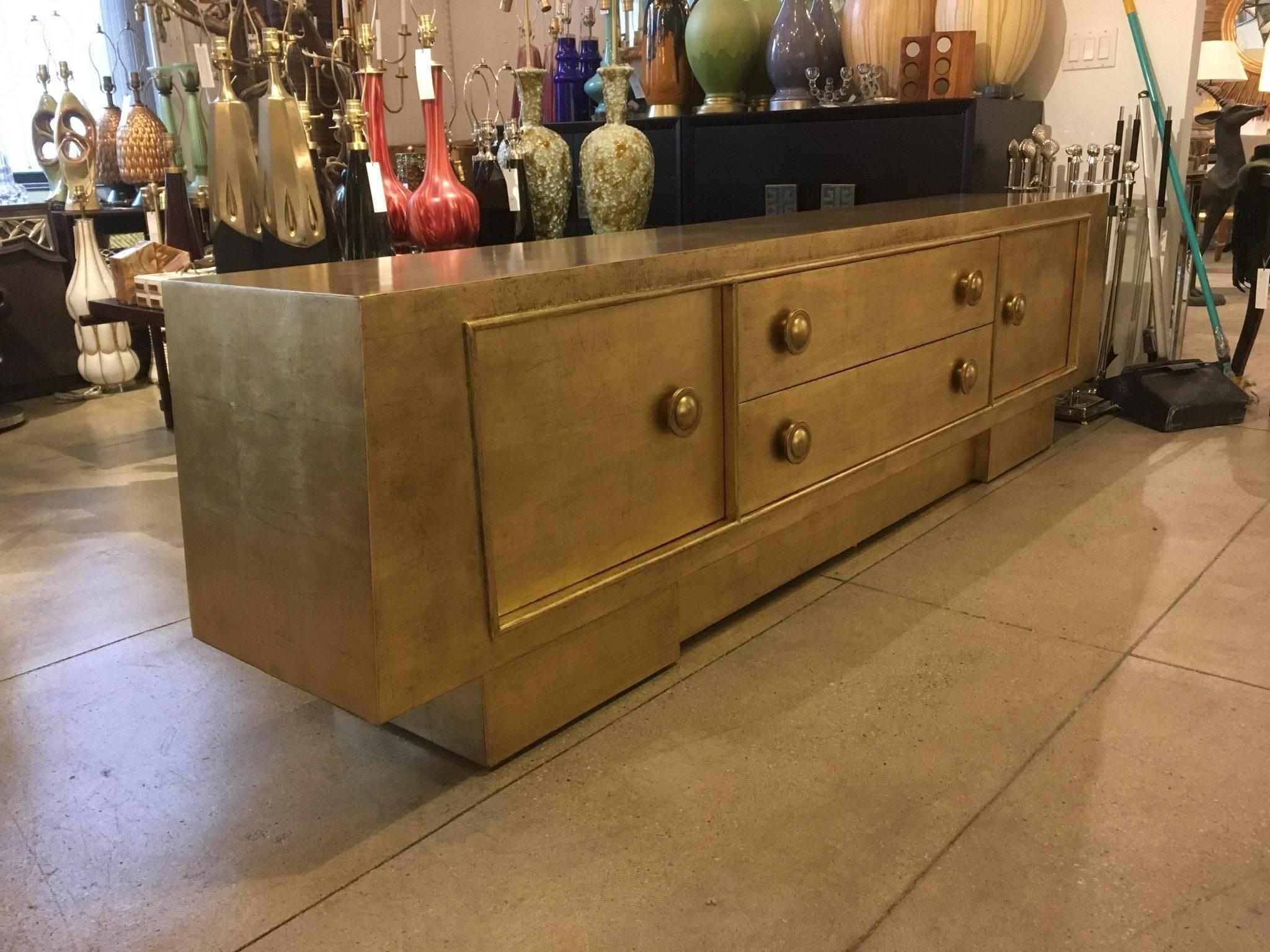 Spectacular Gold leaf credenza with a slight trapezoid shape with 2 large drawers and compartments. Drawers feature large Mont signature button pulls, top drawer branded James Mont Design. 