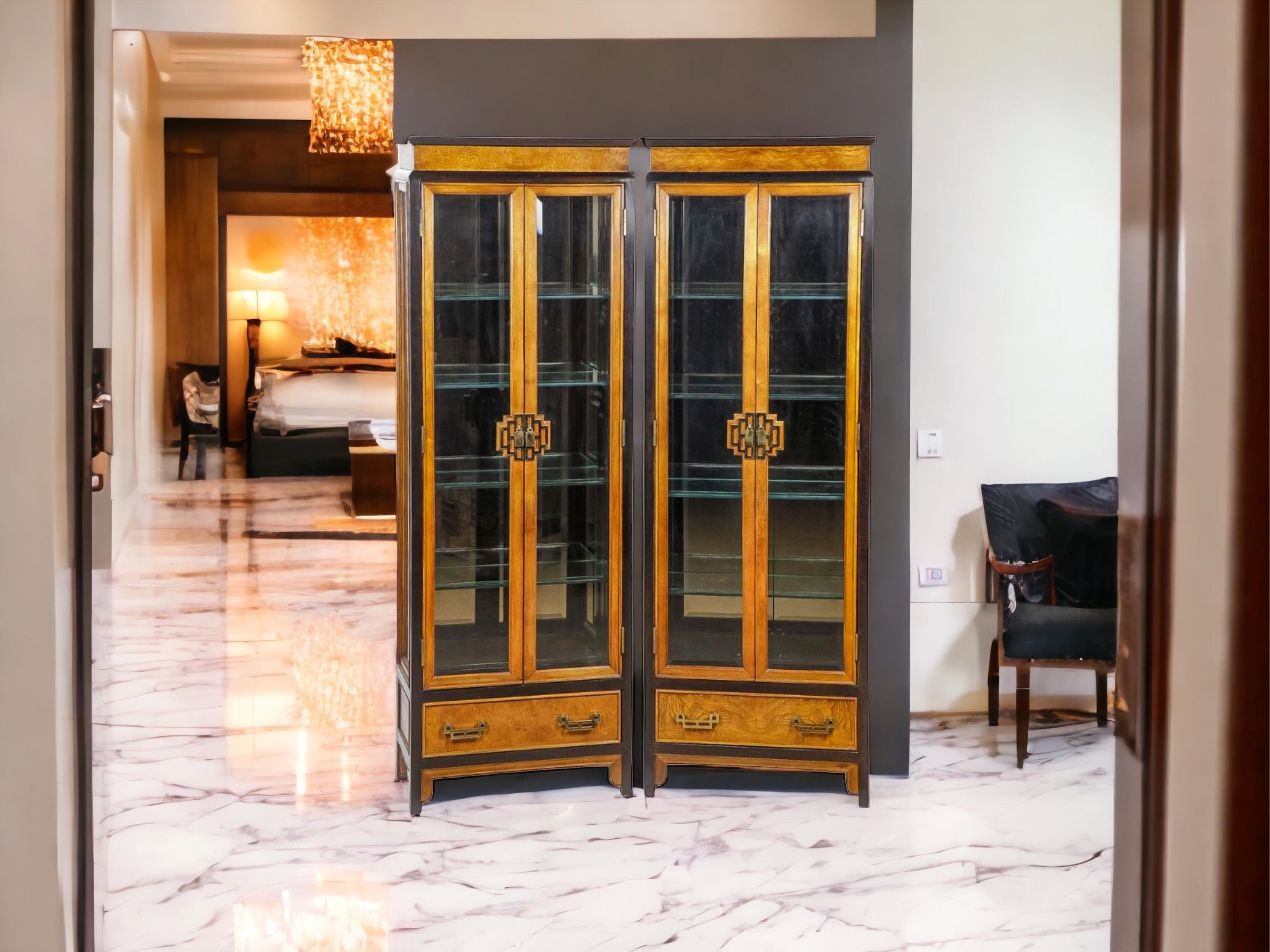 These are a good looking pair of James Mont Asian modern style burl and brass vitrines or display cabinets. They were manufactured by Century. The cabinets of a lit interior and four glass shelves. They are marked and in very good condition. They