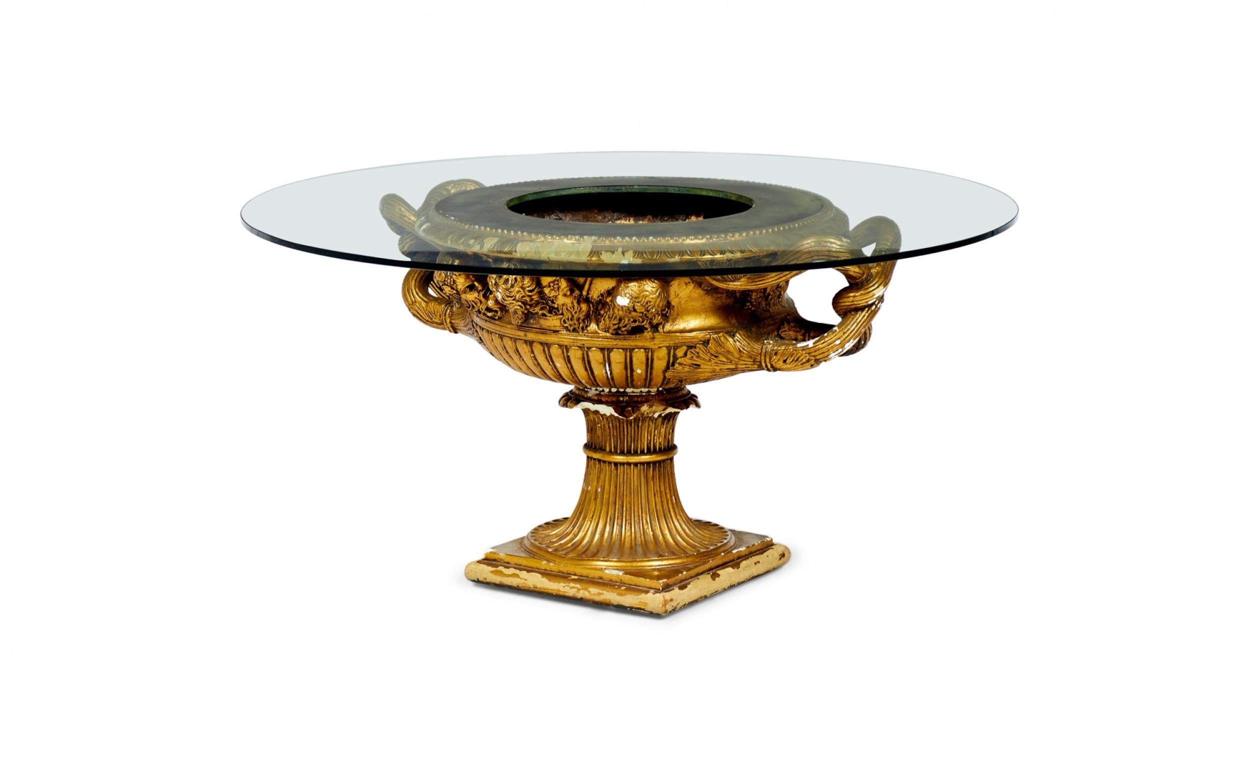 Table basse en forme de jardinière du milieu du siècle dernier (vers 1940), composée d'une urne en plâtre doré surmontée d'un plateau circulaire en verre avec une ouverture centrale arrondie pour accueillir une plante. (JAMES MONT)

Éclats