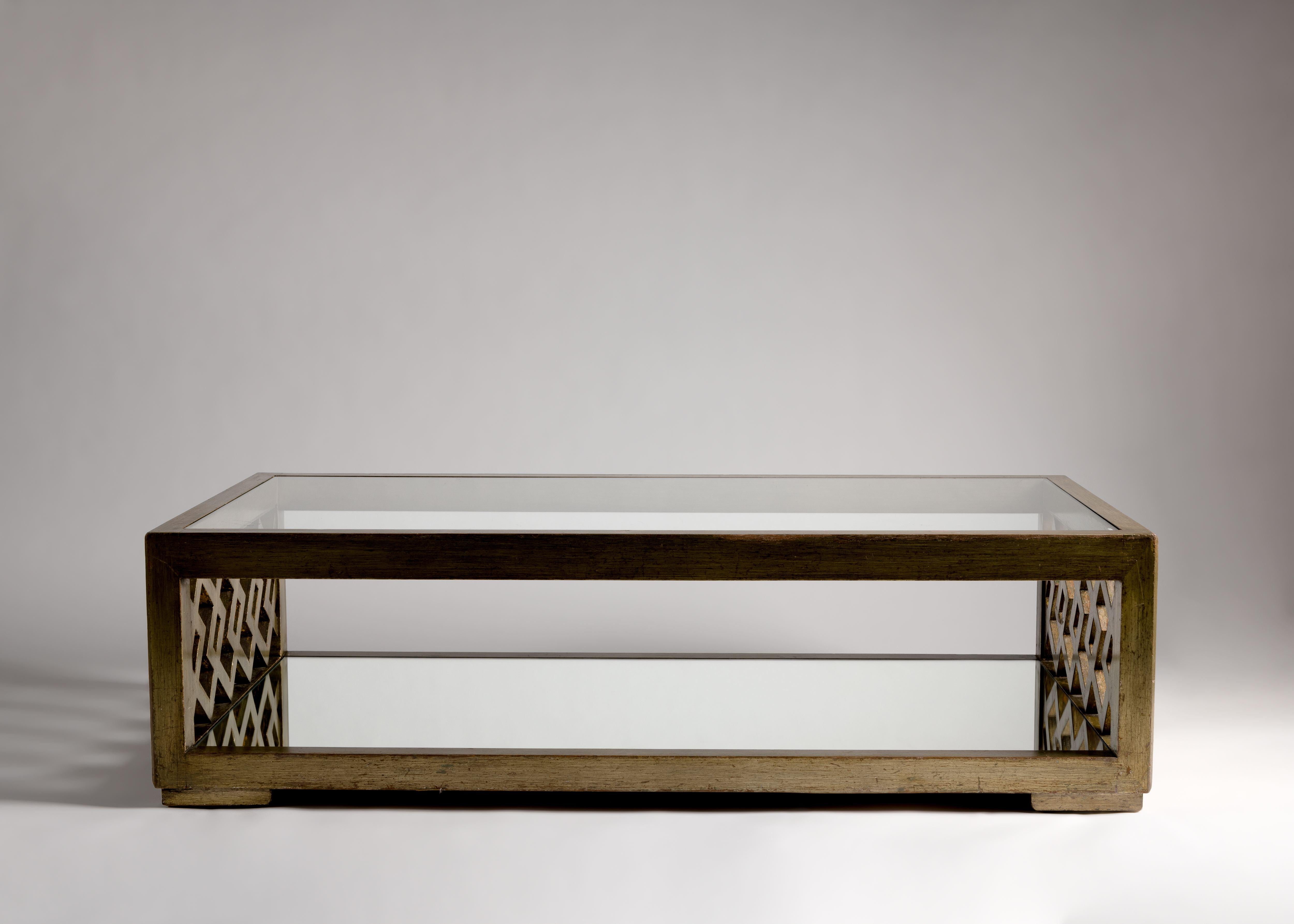 This remarkable coffee table features ends in playful, repeating geometric patterning, which like the rest of its frame, are covered in antiqued silver leaf. Moreover, it boasts two levels -- the top, a broad clear glass, and the bottom a mirror of
