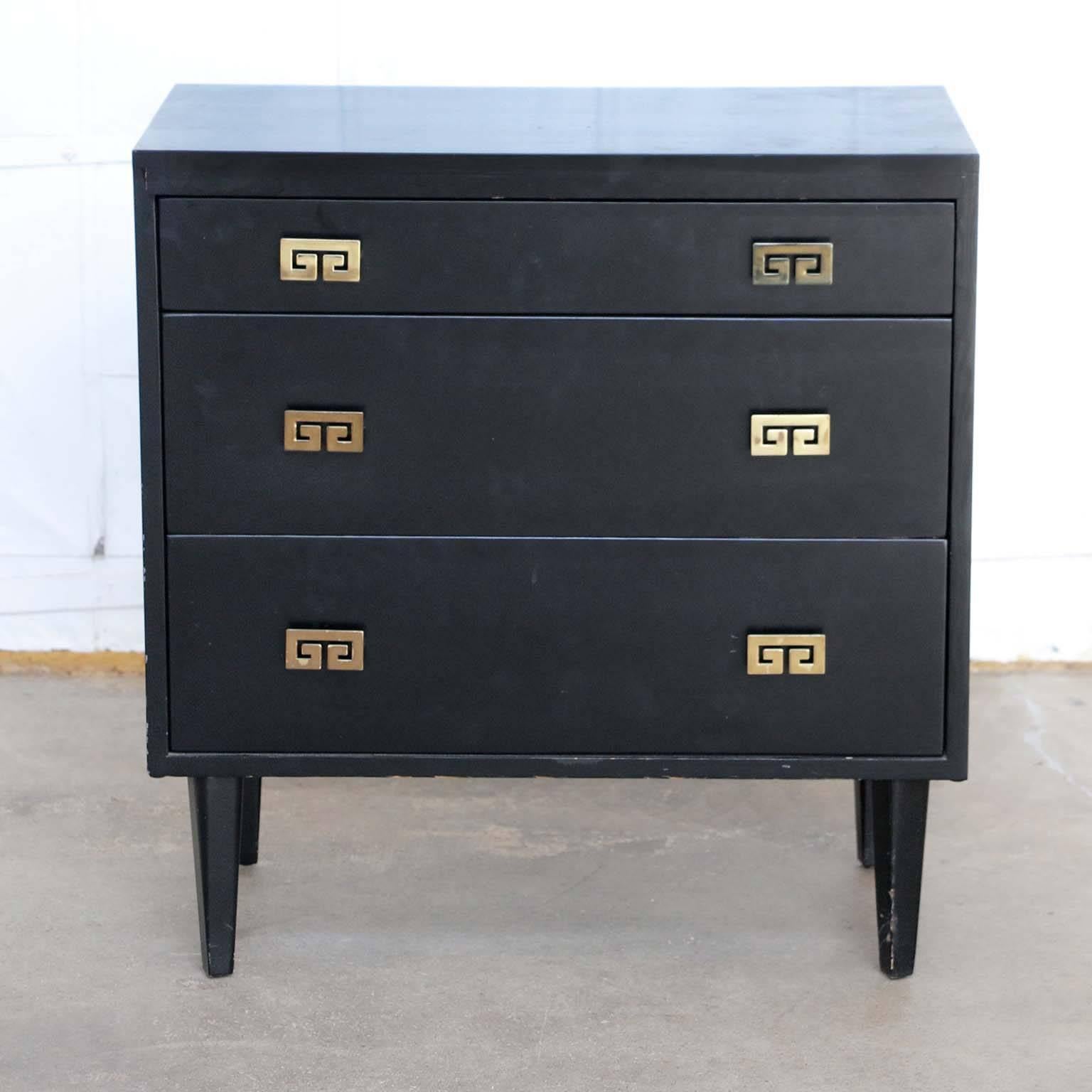 Elegant Mid-Century Modern ebonized three-drawer dresser or chest of drawers. Made in the manner of James Mont by Woodland of California. Featuring a black finish with decorative brass pulls in a Greek key motif. The dresser is supported by tapered
