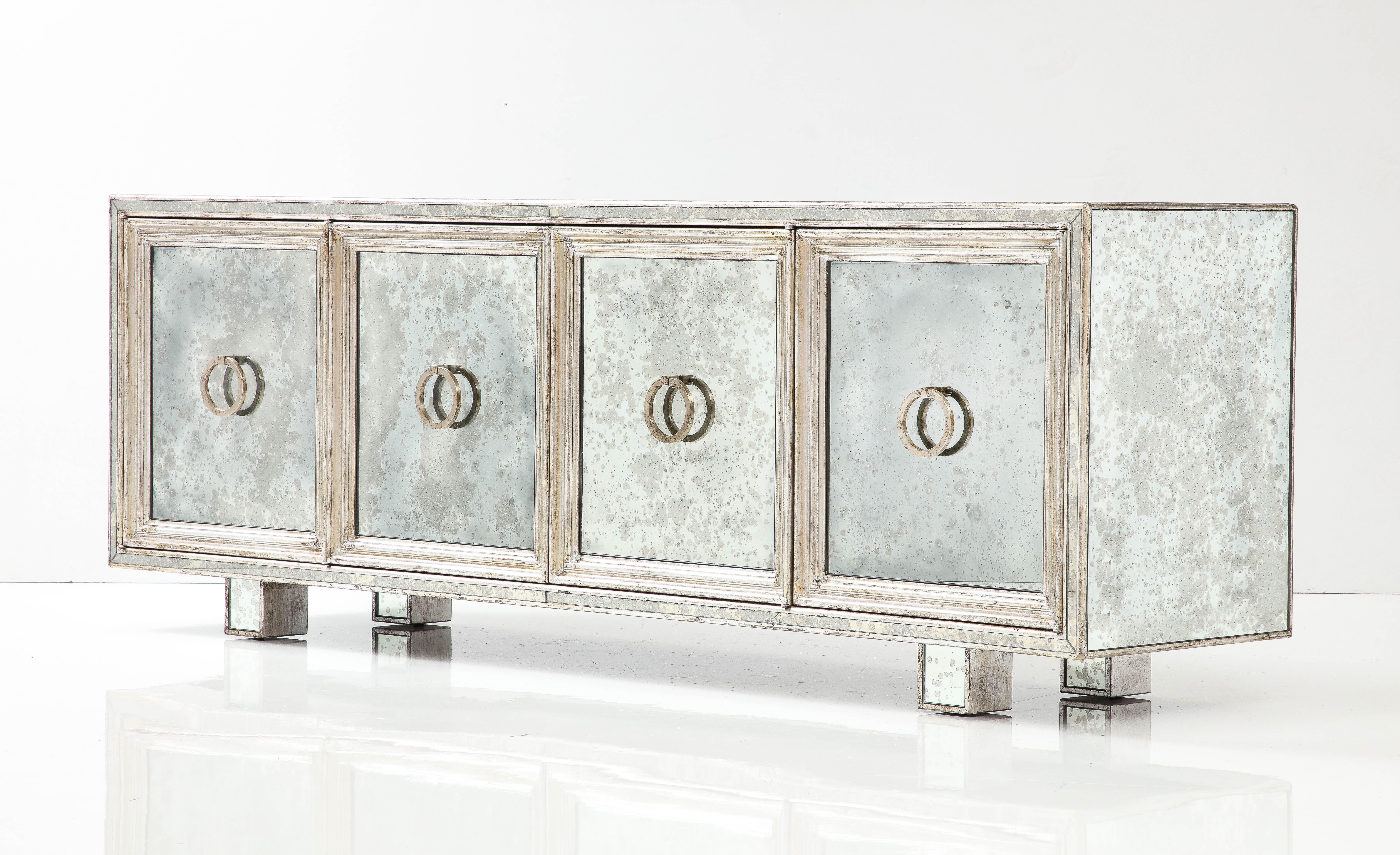 Custom made Art Deco influenced mirrored and silver leaf credenza featuring 4 panels with pulls which conceal 3 ample storage compartments. Each compartment housing 1 adjustable shelf. Style of James Mont.