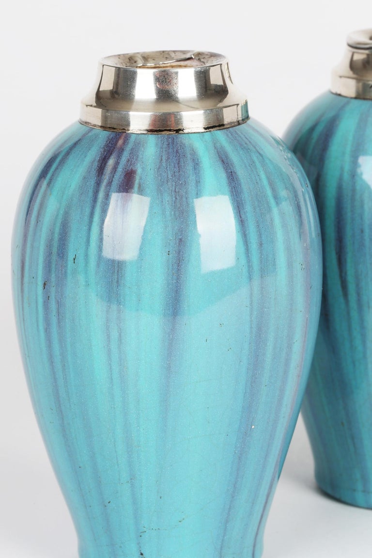 An unusual pair Art Deco silver mounted art nouveau vases decorated in turquoise streaked glazes by James Plant & Sons and dating from the early 20th century. The bulbous shaped earthenware vases stand on a narrow rounded base with a raised rounded