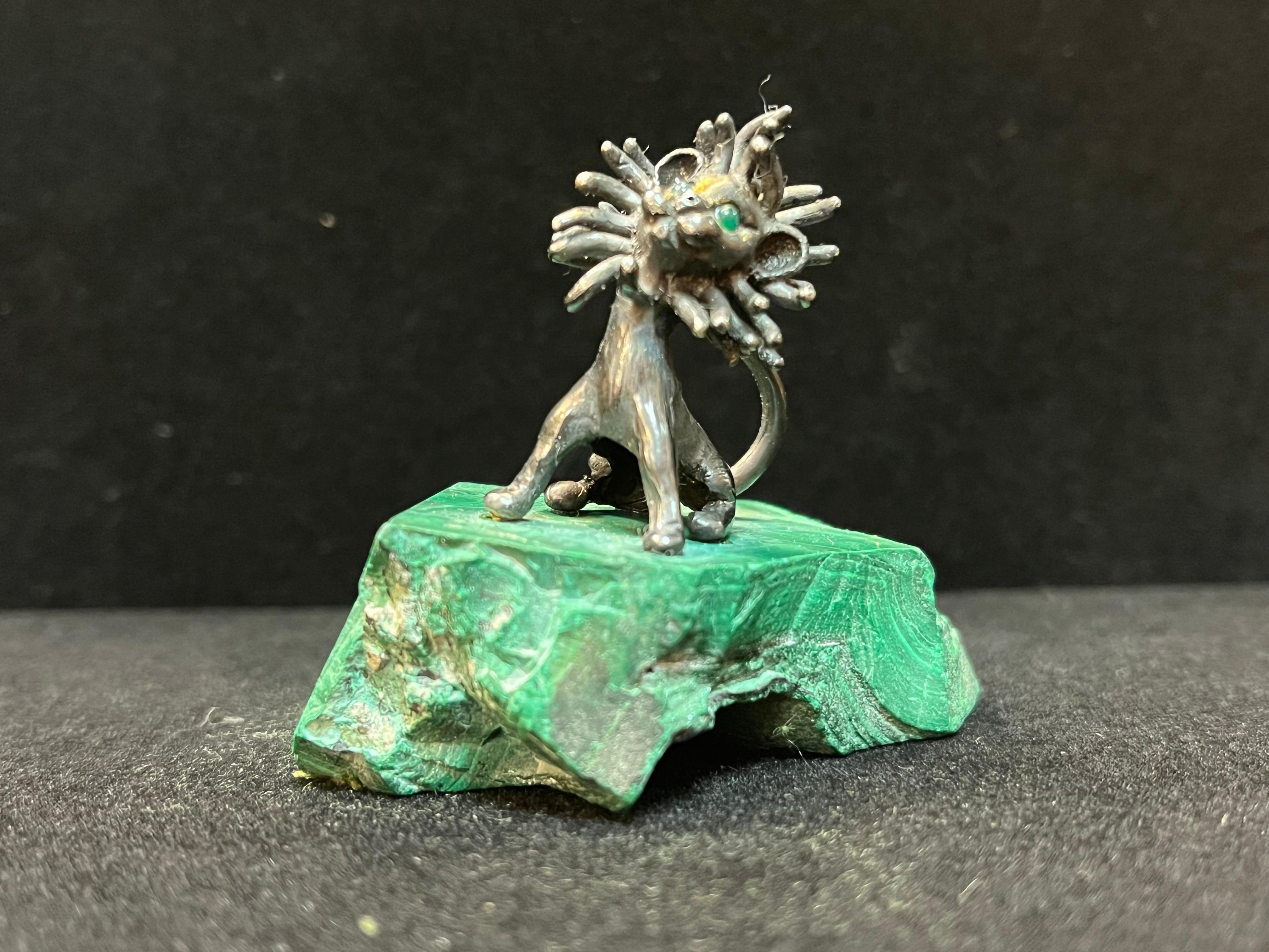 A sterling silver sculpted lion by late American artist James Schwabe (1918 - 2008) mounted onto malachite. The eyes of the lion are gemstone (possibly cabochon emerald) and there appear to be highlights in a golden metal. The sculpture is signed on