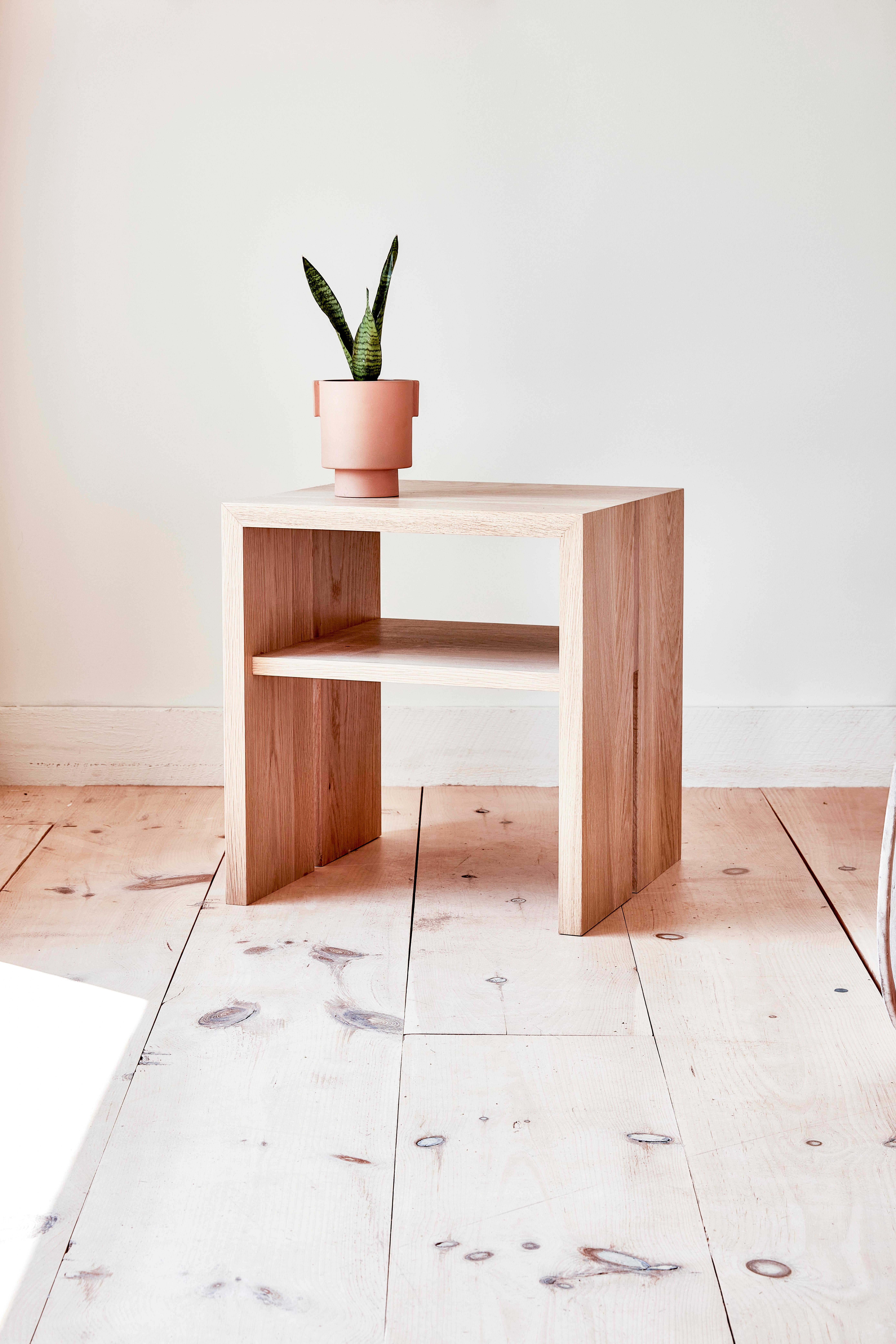 This wooden side table is hand-made in the United States with all hardwood construction. Characterized by its striking waterfall design, unique split leg detail, and convenient storage shelf, the Jameson natural wood side table is distinguished with