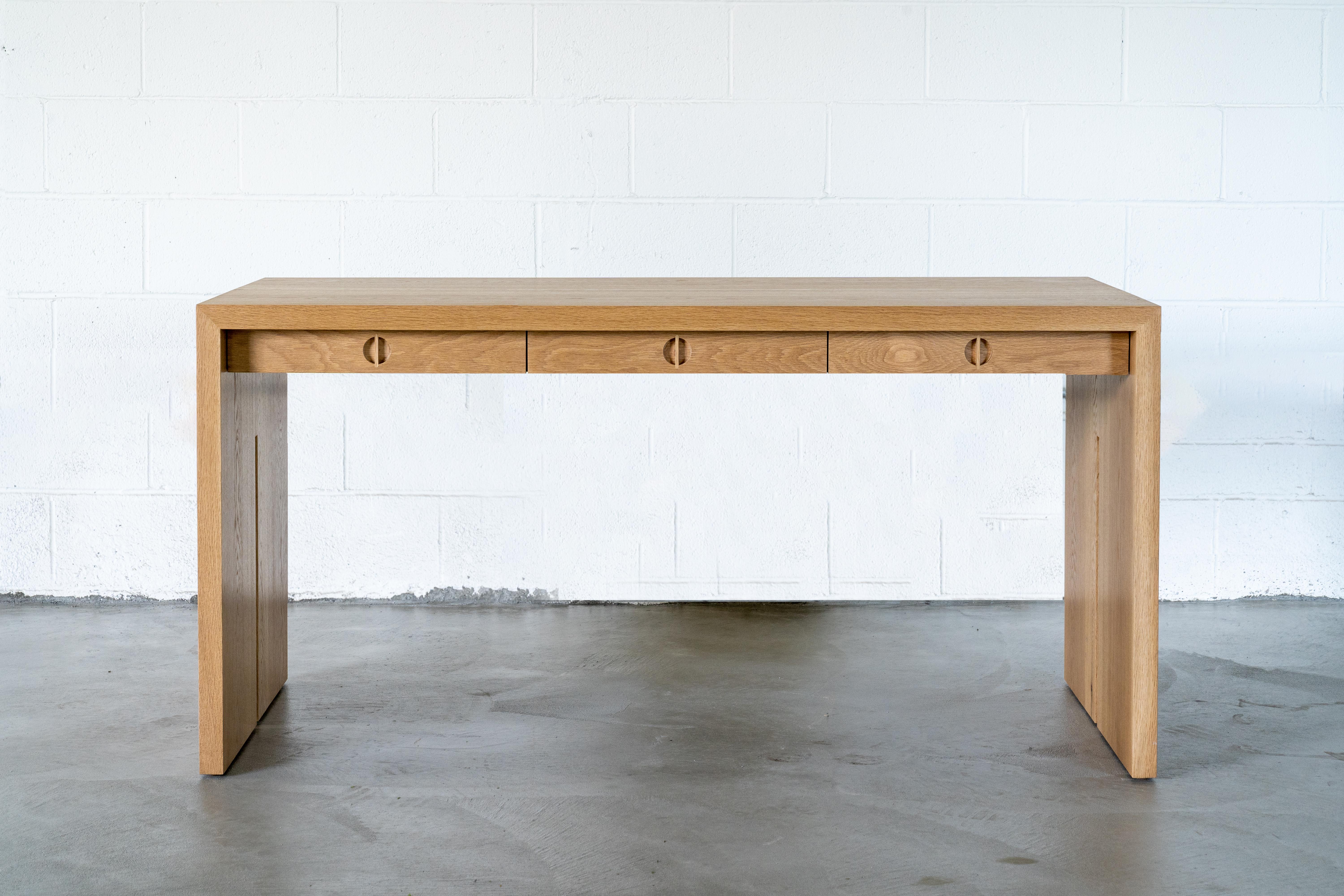 This custom wood desk is hand-made in the United States with all hardwood construction. This modern design is characterized by its solid white oak body, minimalist walnut inlay detail, and unique split leg detail. Convenient and accessible storage