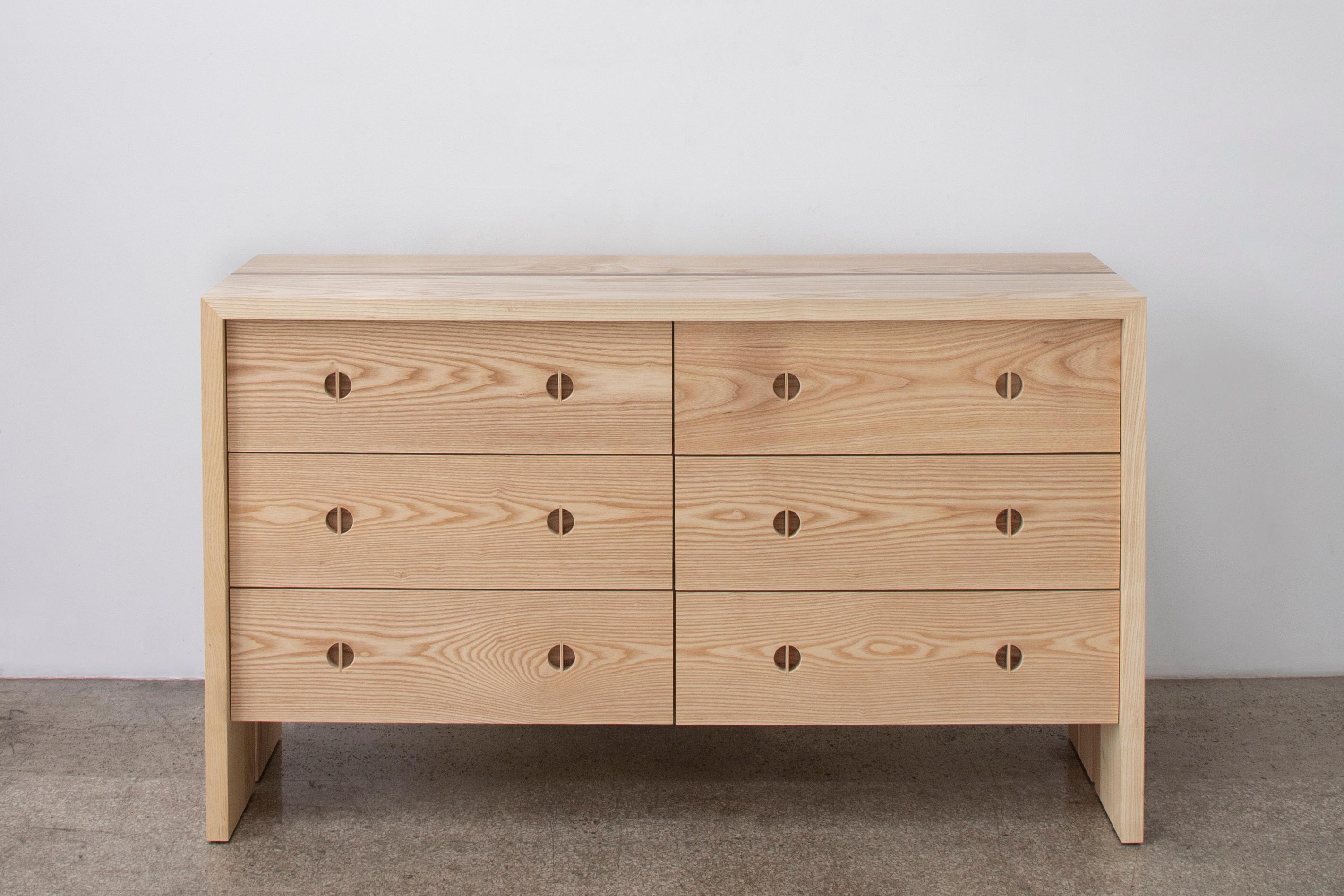 This modern wood dresser is hand-made in the United States with all hardwood construction. Characterized by its solid ash wood body, minimalist walnut inlay detail, and unique split leg detail this contemporary wood dresser has deep storage drawers