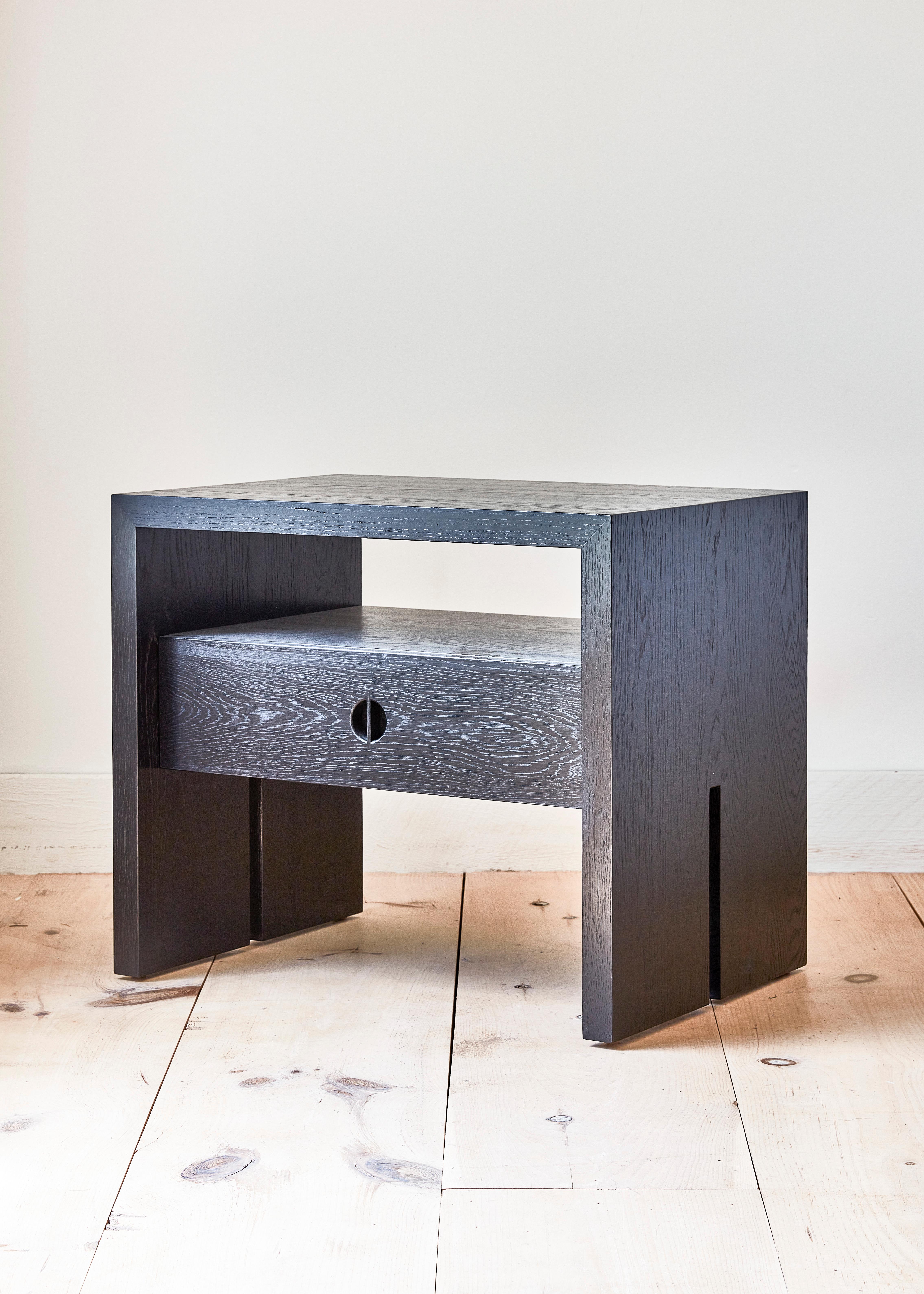This custom wood nightstand is hand-made in the United States with all hardwood construction. Characterized by its striking waterfall design, unique split leg detail, and convenient and accessible storage drawer, the minimalist Jameson bedside table