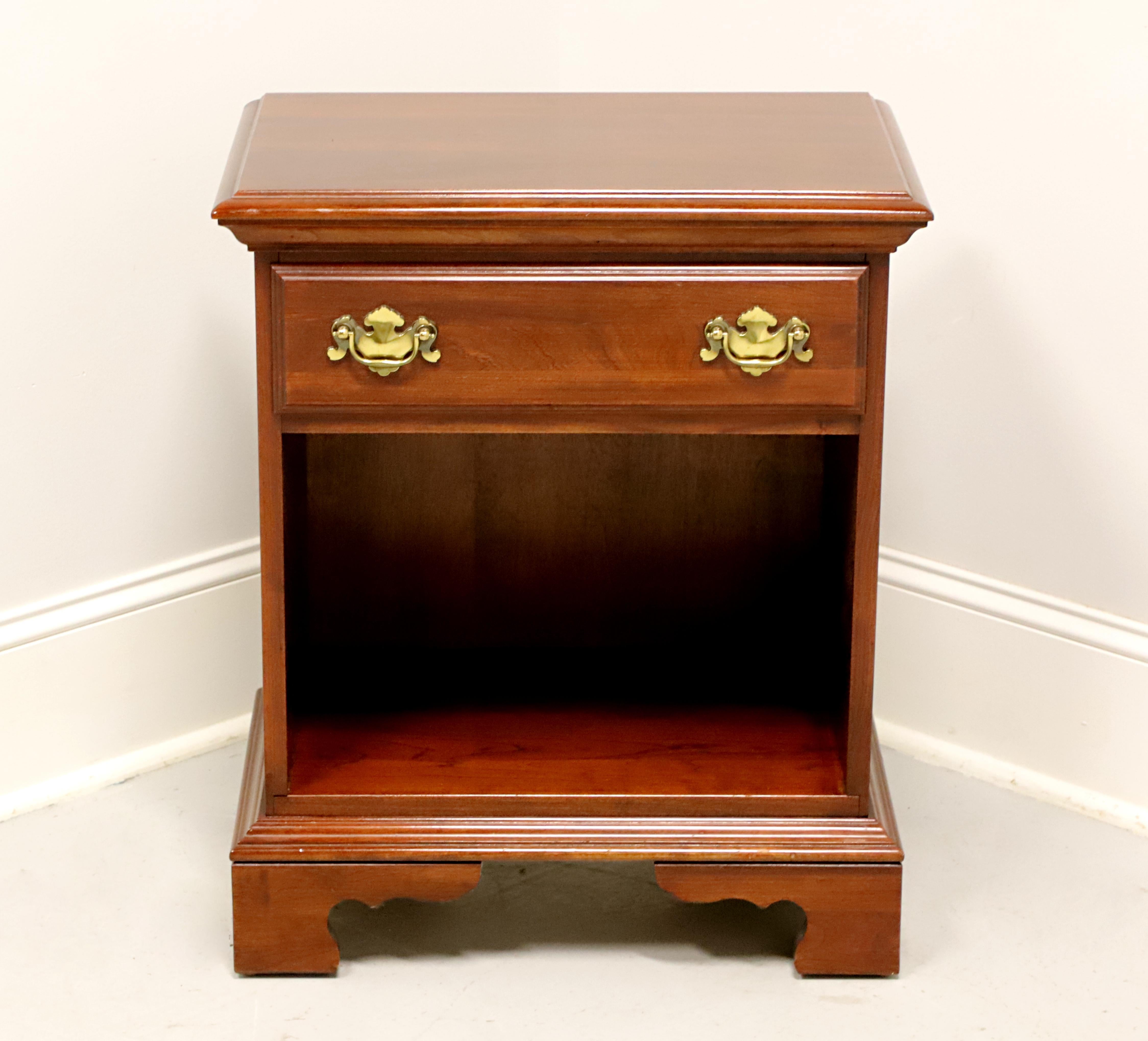 A Chippendale style bedside chest by Jamestown Sterling. Cherry with brass hardware, ogee edge to the top, and bracket feet. Features one drawer of dovetail construction over an open shelf storage area. Made in the USA, in the late 20th