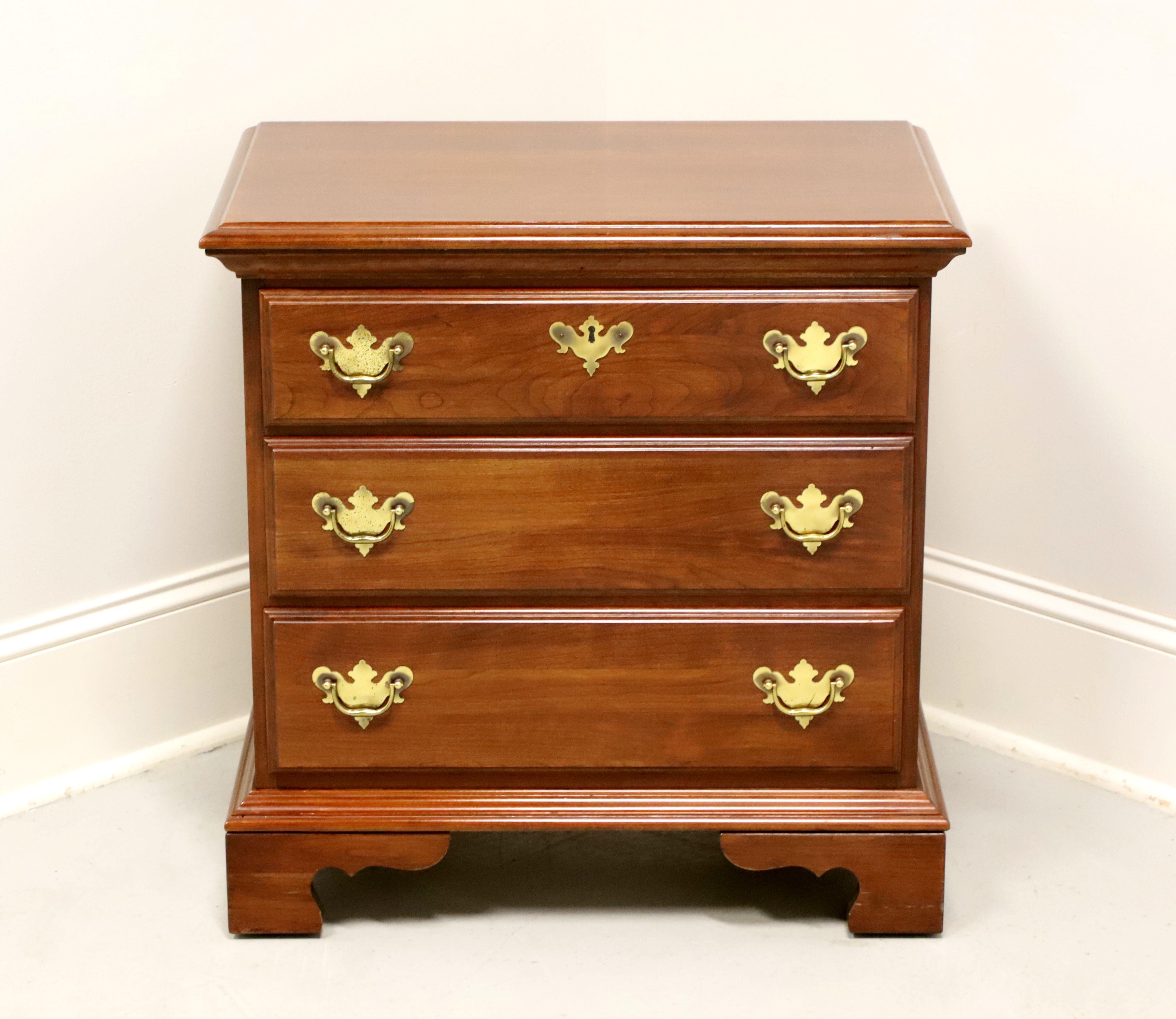 A Chippendale style bedside chest by Jamestown Sterling. Cherry wood with brass hardware, ogee edge to the top, and bracket feet. Features three drawers of dovetail construction, top drawer having a faux keyhole escutcheon. Made in the USA, in the